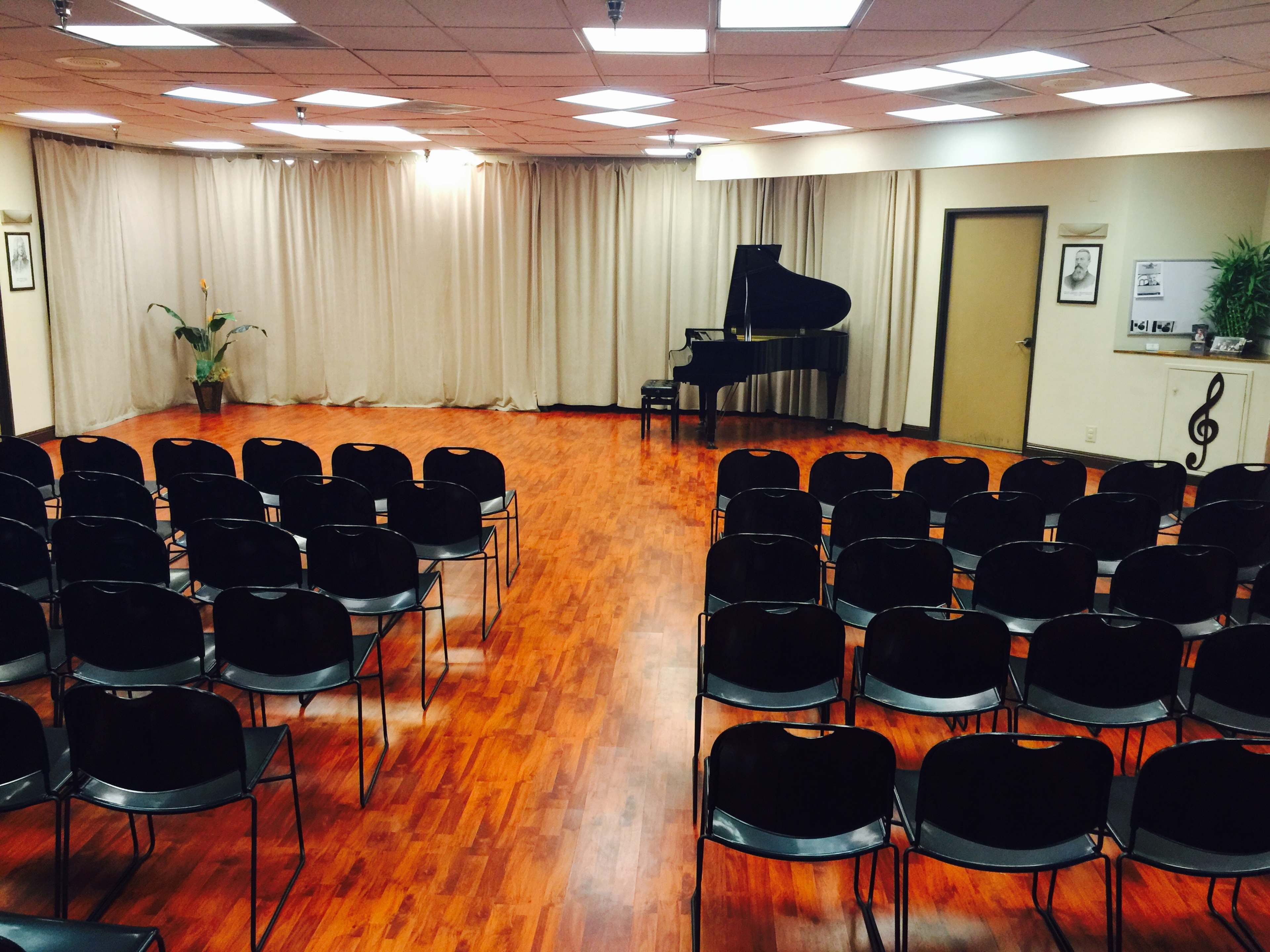 A music performance room with rows of black chairs facing a grand piano and a curtain backdrop.