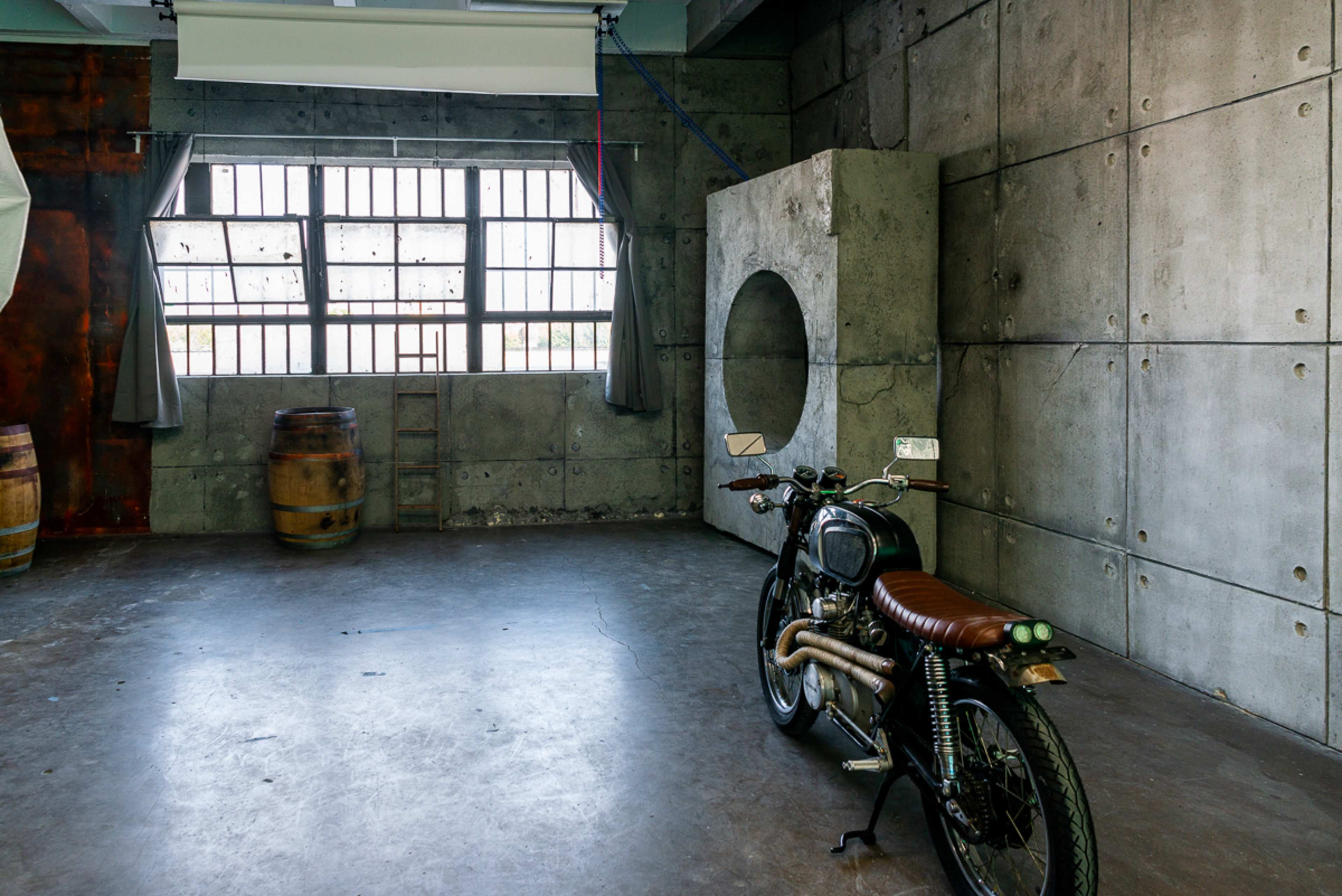 A vintage motorcycle is positioned in a spacious room featuring concrete walls and large windows.