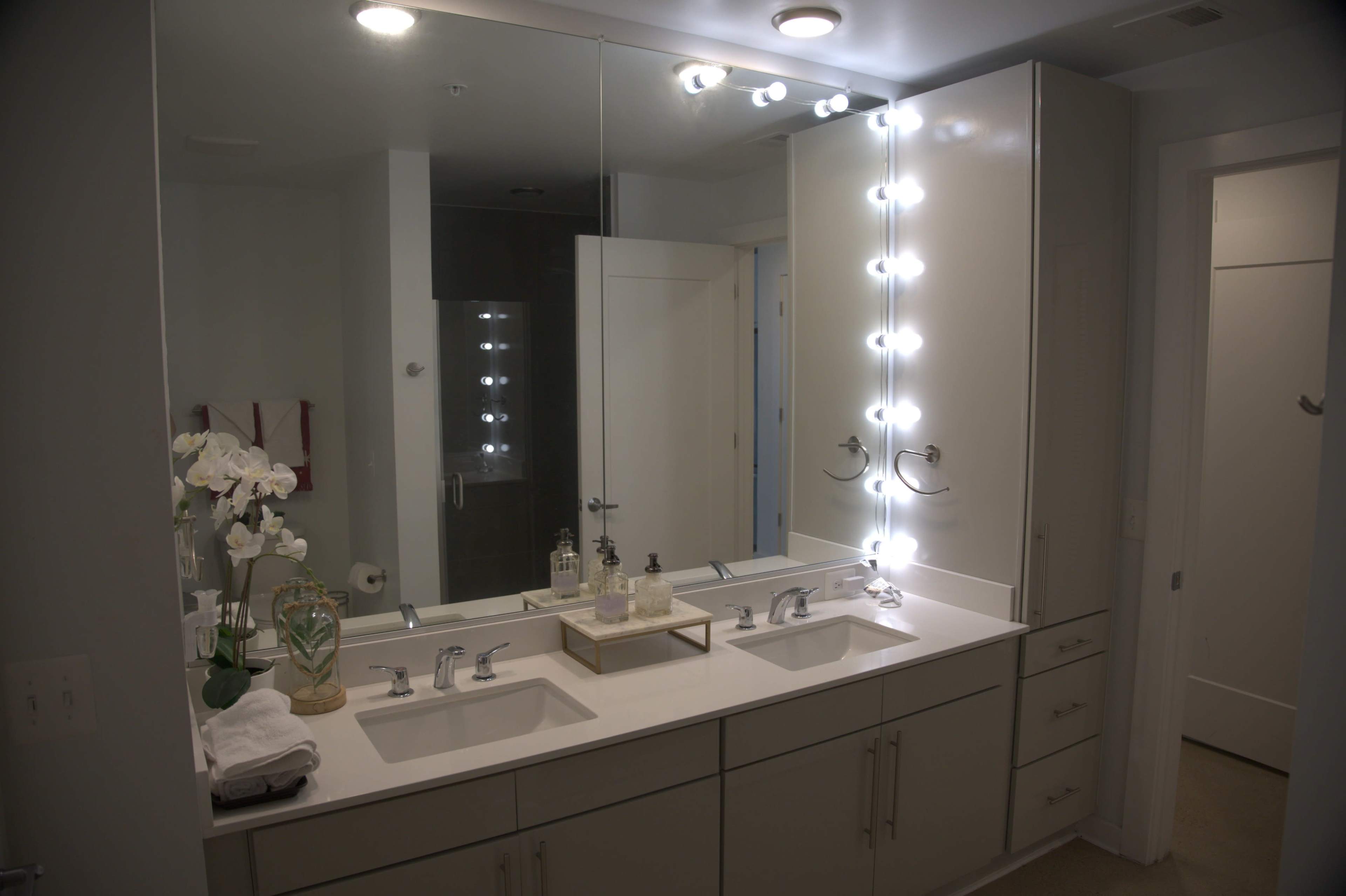 A modern bathroom with a double vanity, large mirrors, and bright LED lighting.