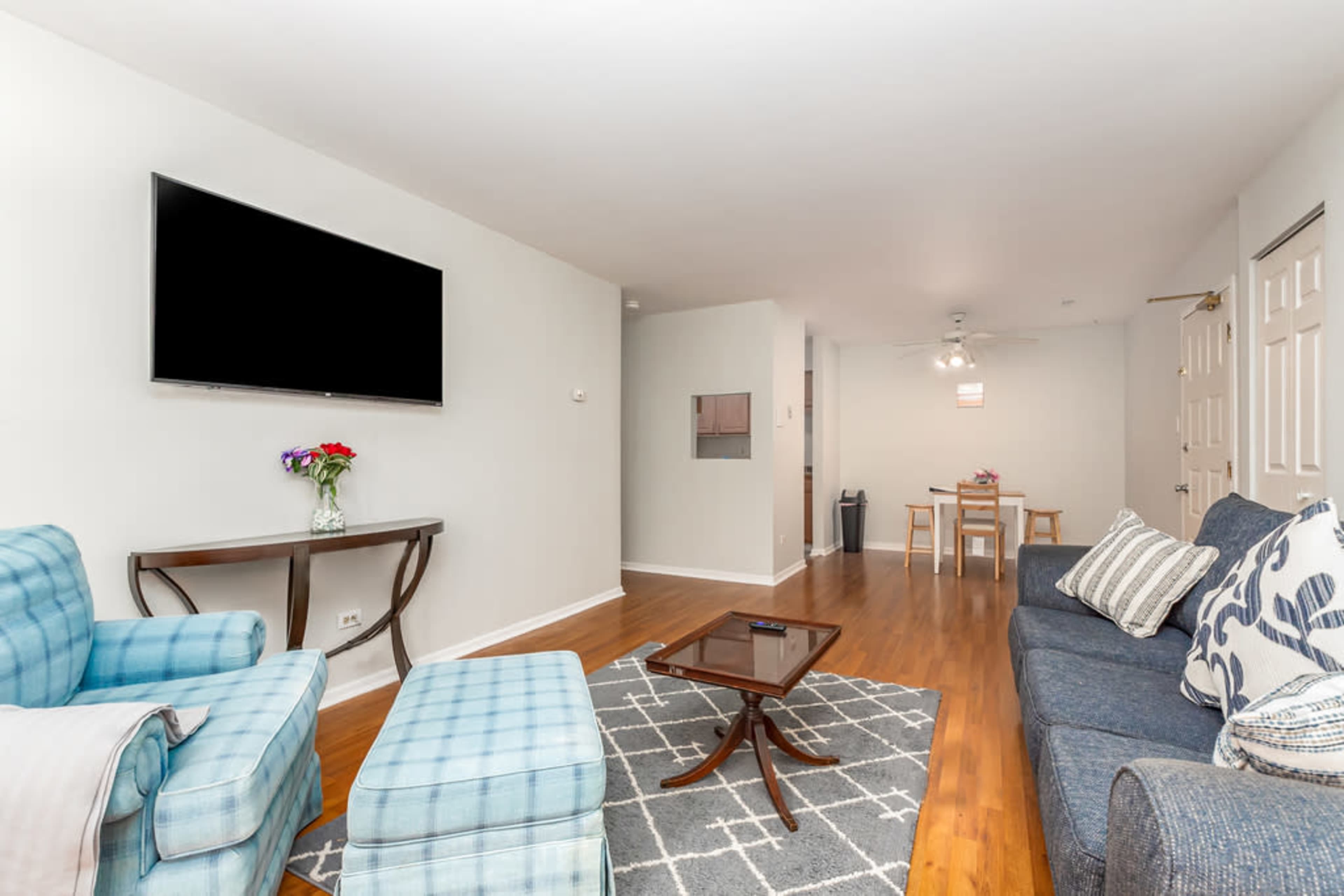 The living area features a television mounted on the wall, two blue chairs, a dark blue sofa, and a dining table in the background.