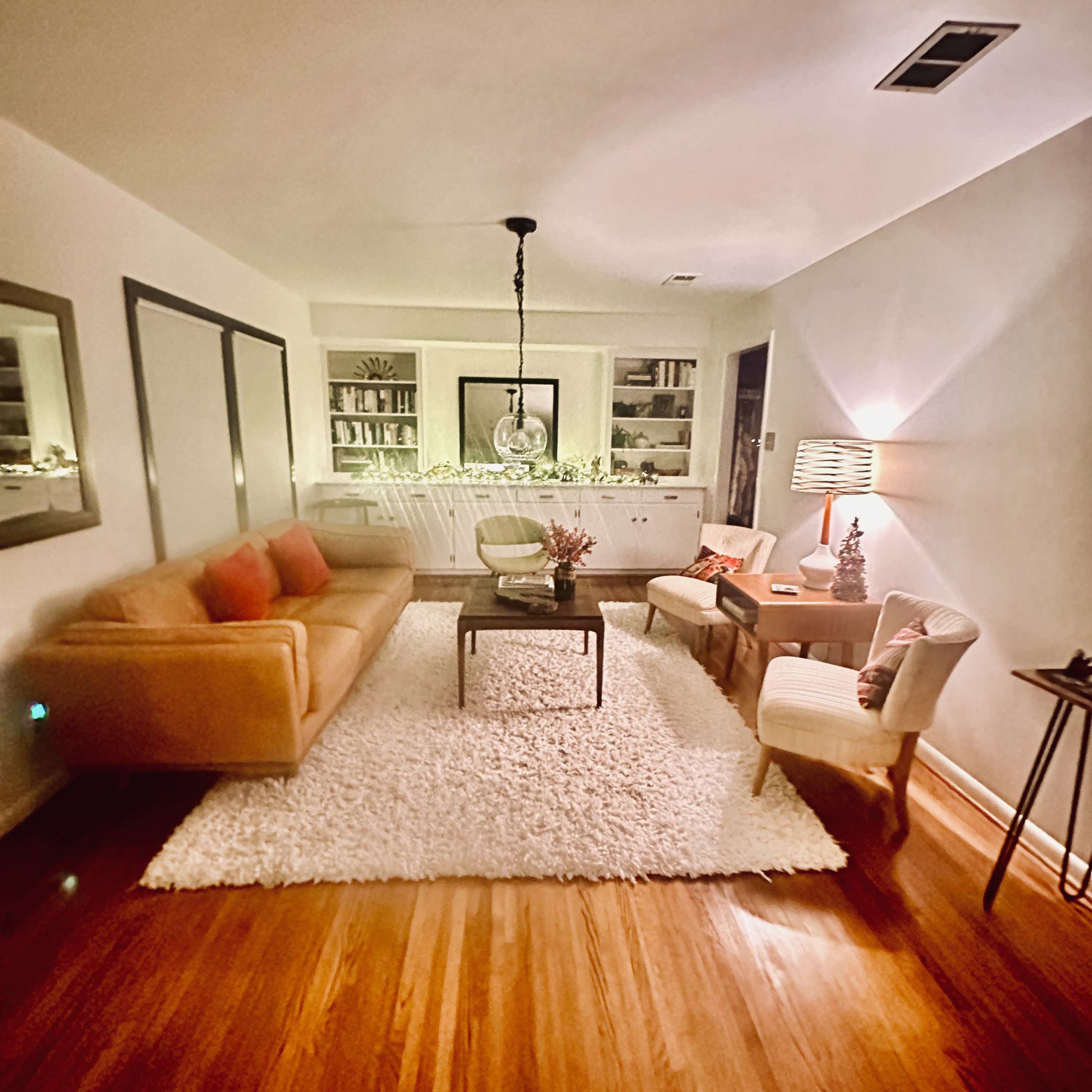 A cozy living room with a sofa, two chairs, a coffee table, and bookshelves against the walls, all on a plush white rug.