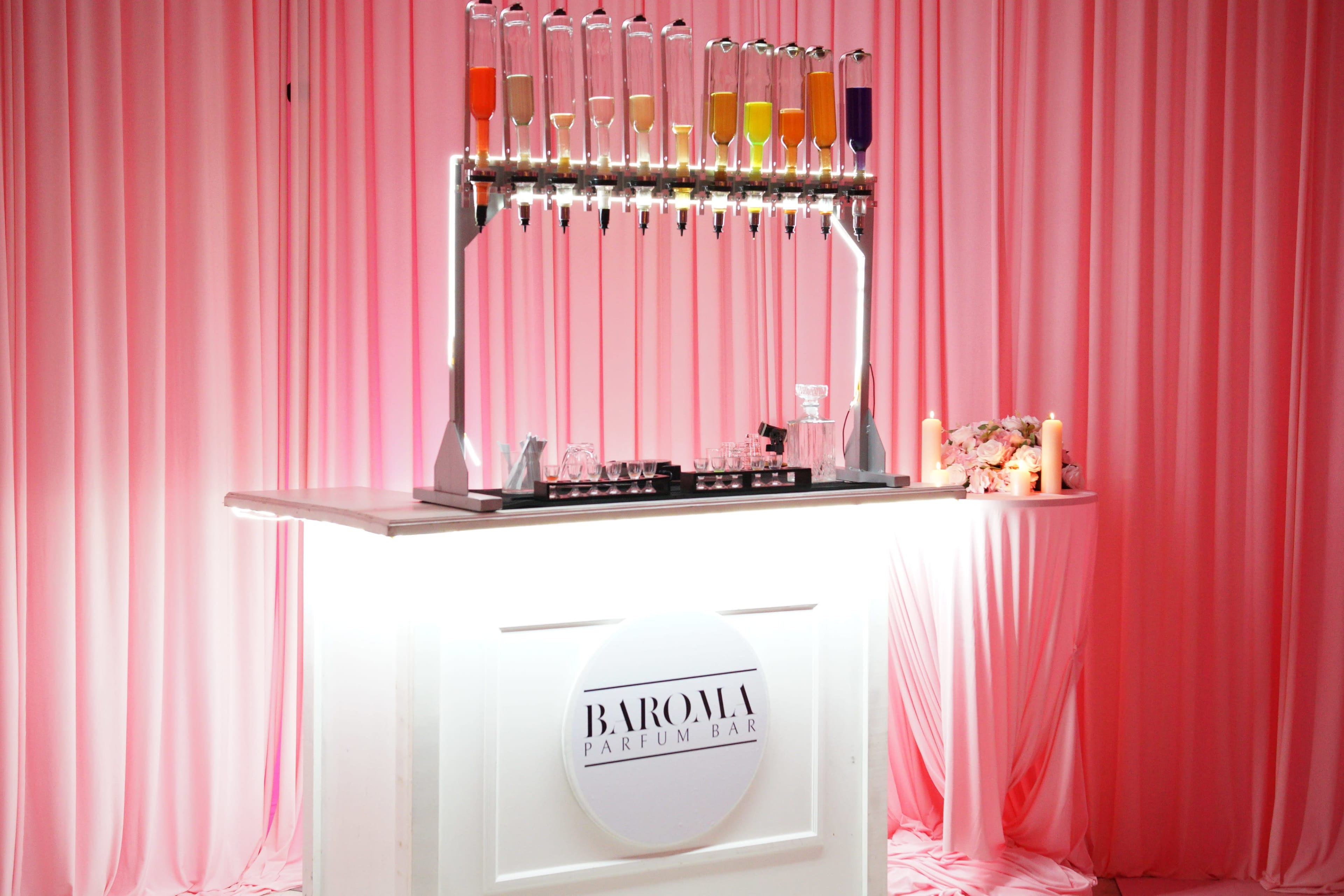 A bar featuring multiple test tubes filled with colorful liquids is set against a pink fabric backdrop.
