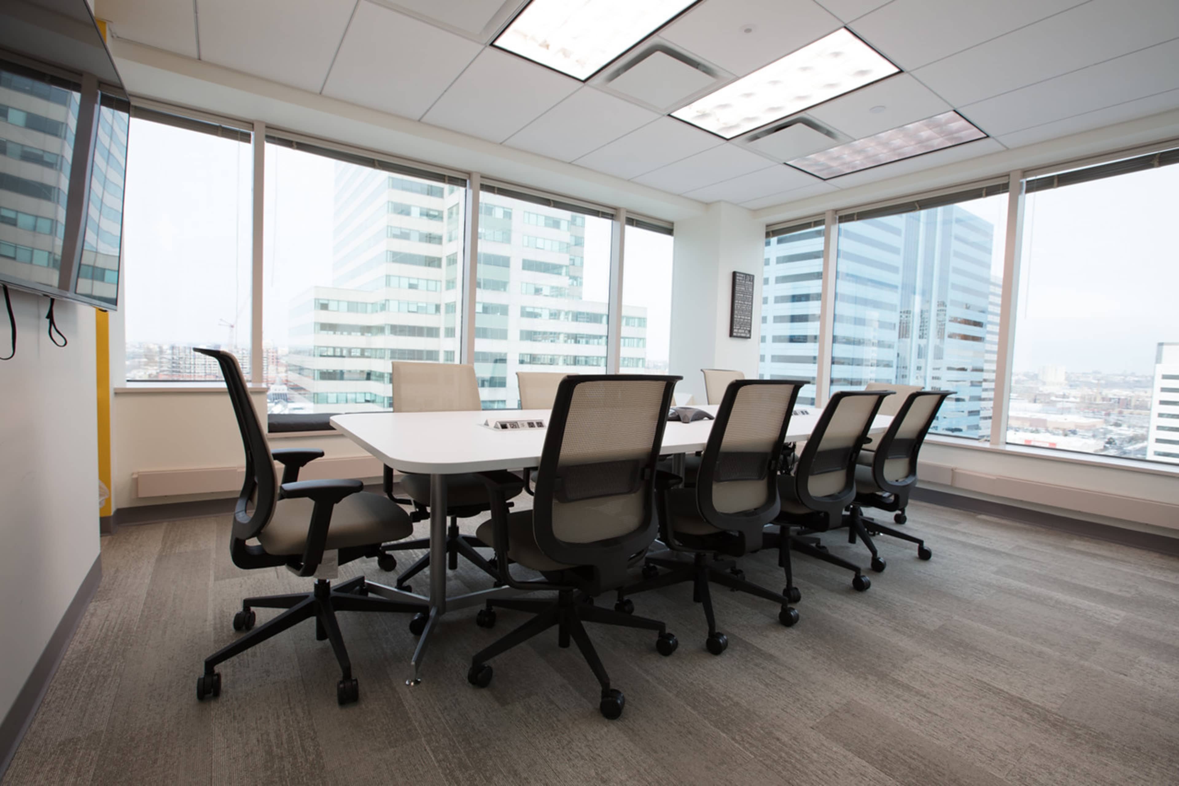 A modern conference room features a large table surrounded by ergonomic chairs, with floor-to-ceiling windows overlooking a cityscape.