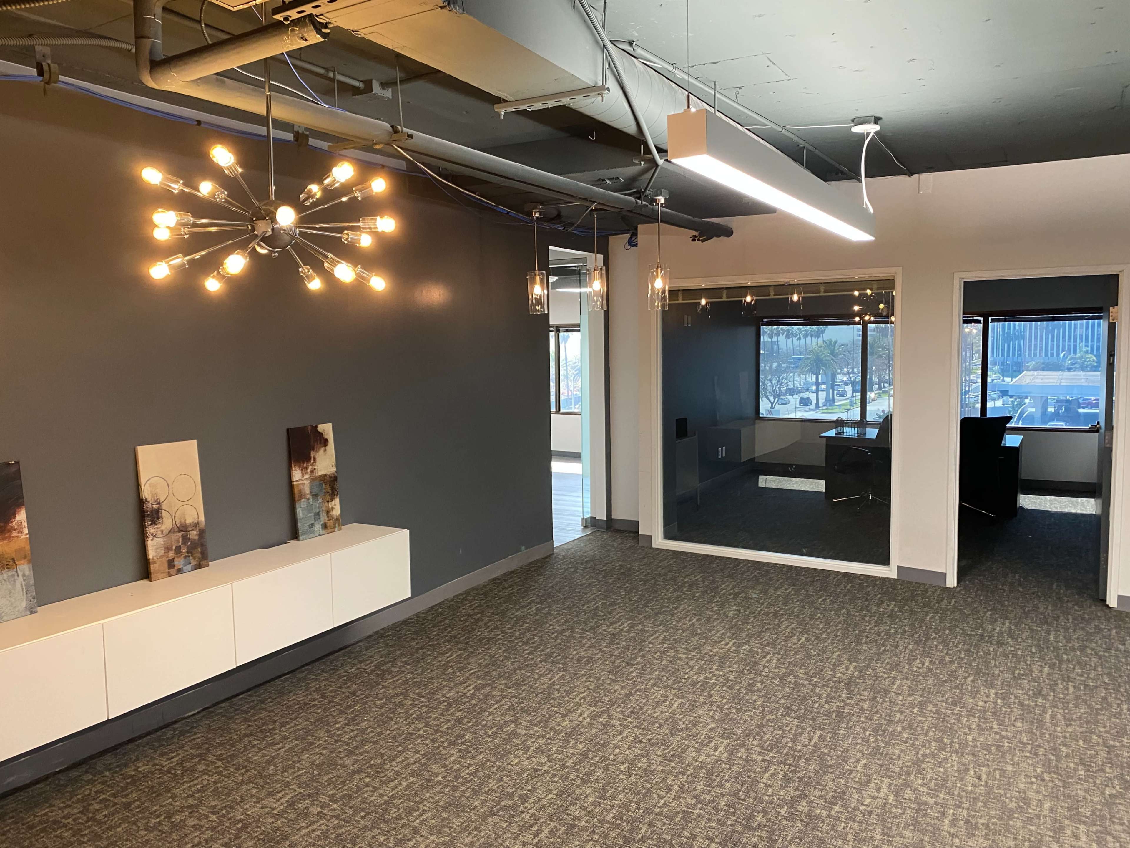 A modern office space featuring a gray wall, a decorative light fixture, and a glass-walled meeting room.