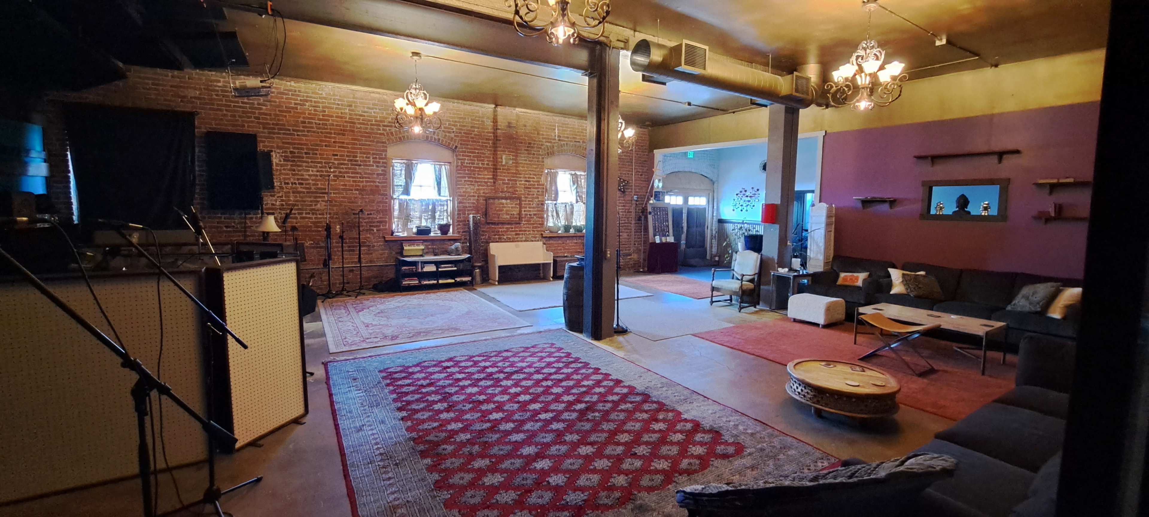 An interior space with exposed brick walls, a mix of seating arrangements, and various lighting fixtures hanging from the ceiling.