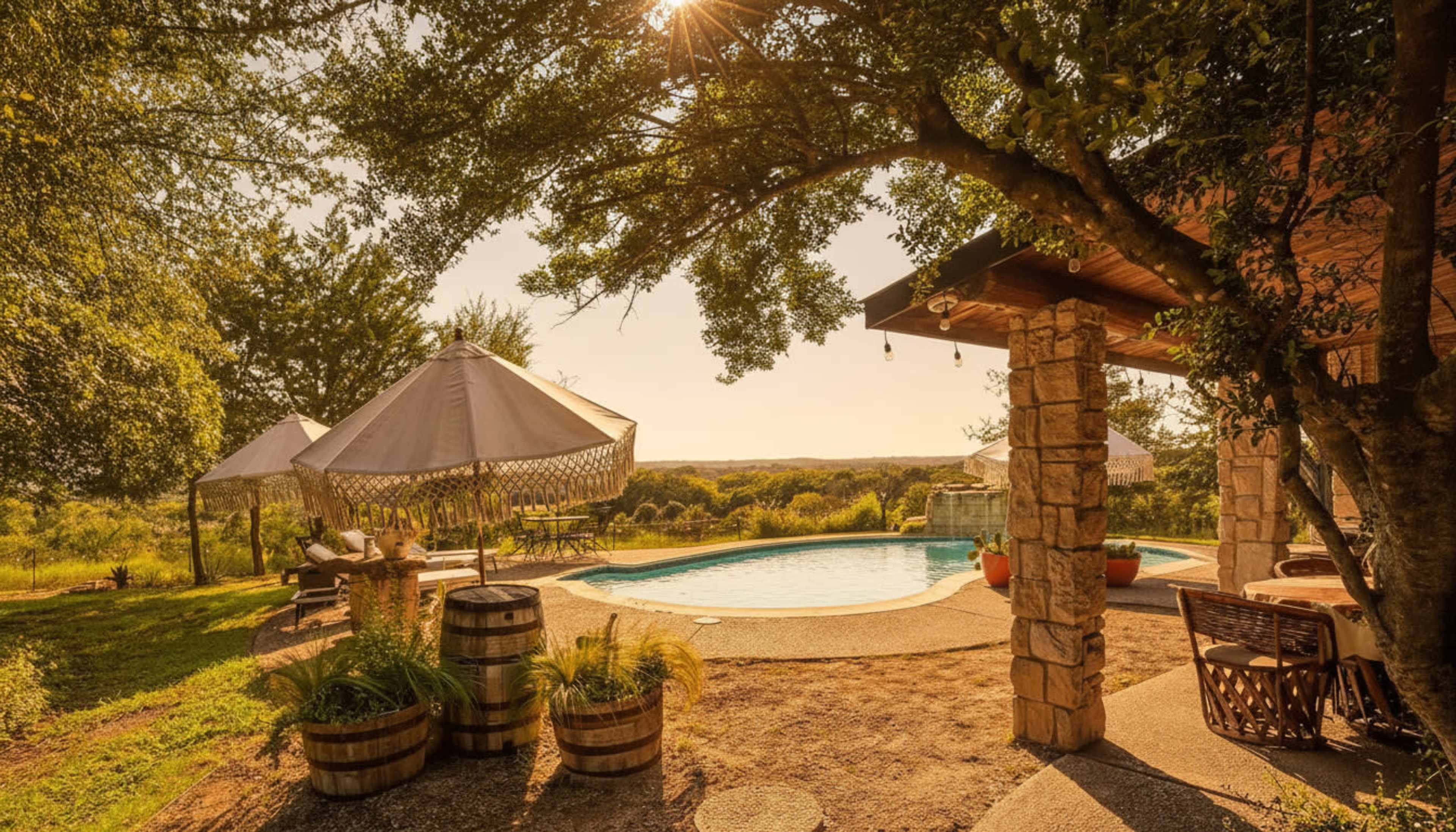 The image shows a landscape with a swimming pool surrounded by wooden barrels, lounge chairs, and a large shaded gazebo, set against a sunset view.