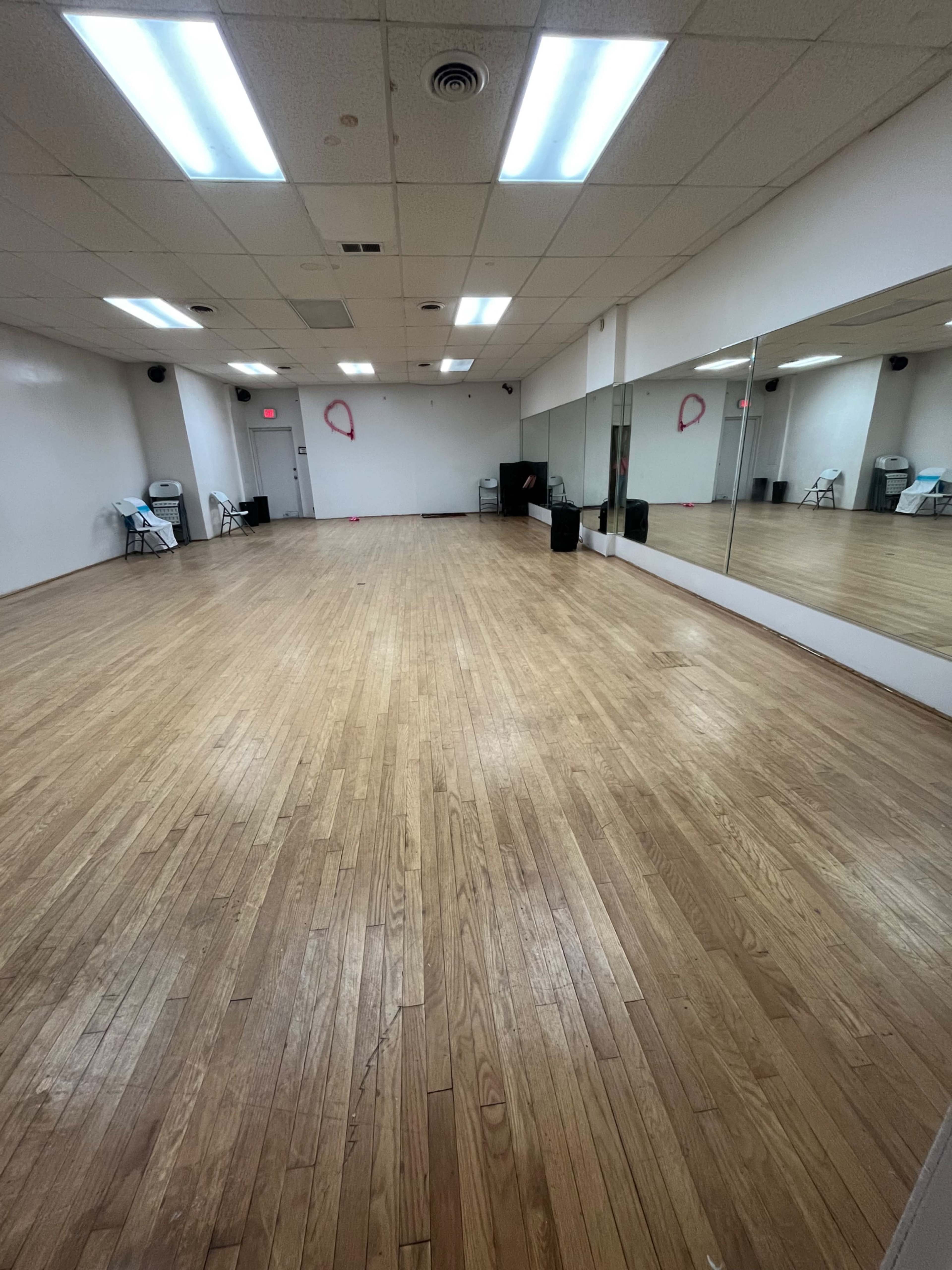 The image shows an empty dance studio with polished wooden floors and mirrors along one wall.
