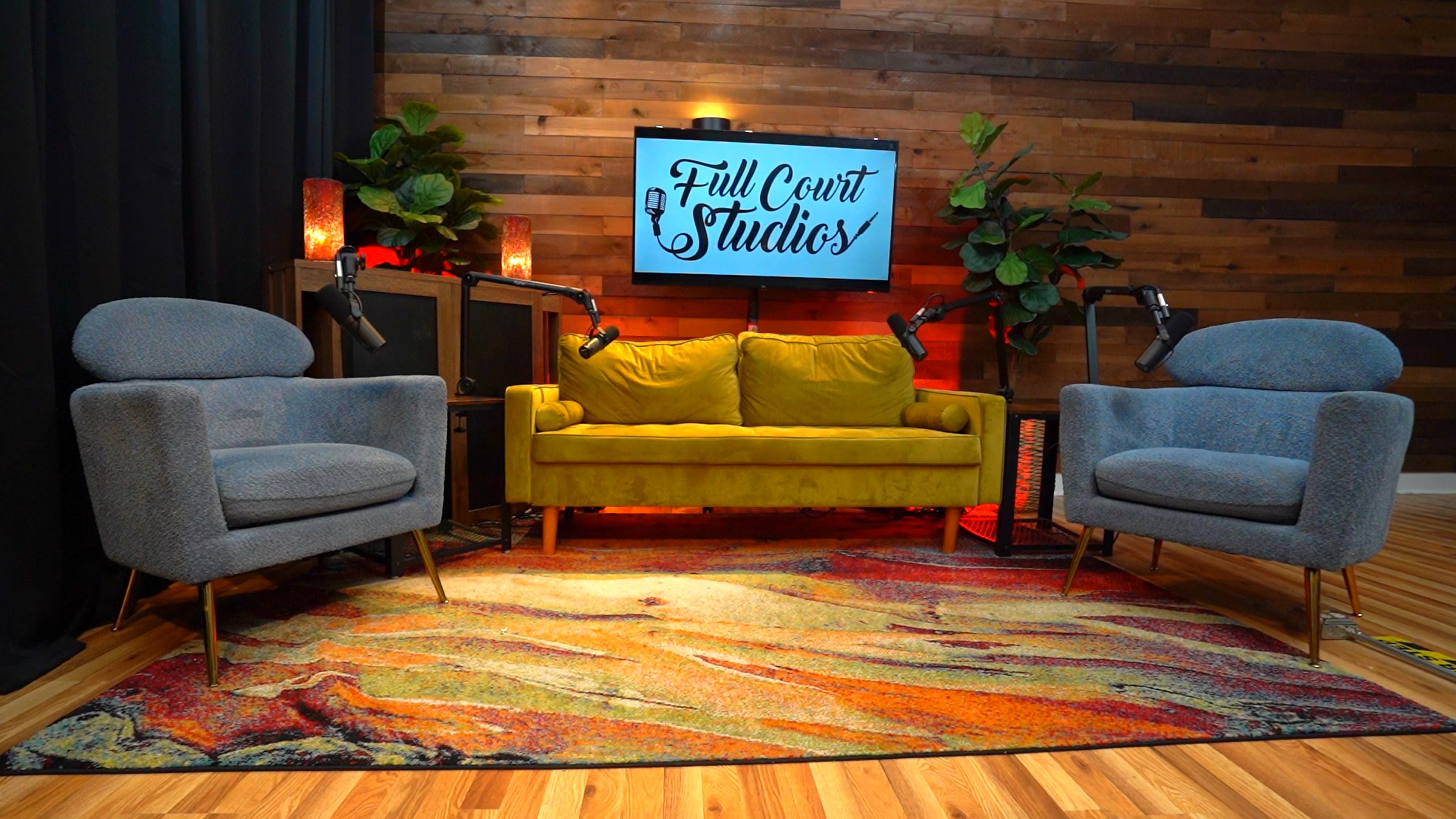 The image features a cozy studio setup with a yellow couch, two gray chairs, and a wooden wall backdrop, illuminated by soft lighting.