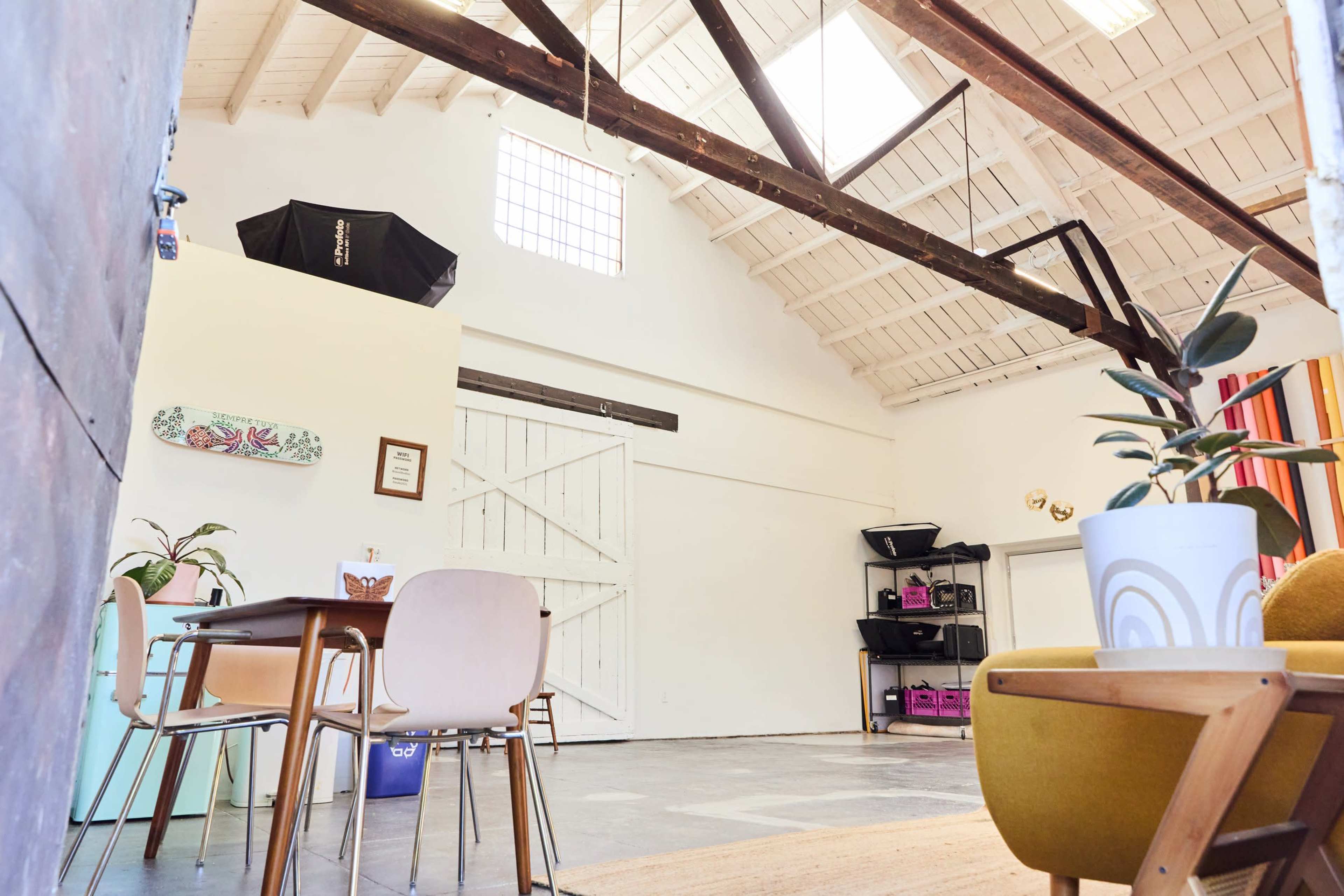 A spacious interior features a dining area with chairs, a wooden table, and a backdrop of tall ceilings, beams, and a large door.