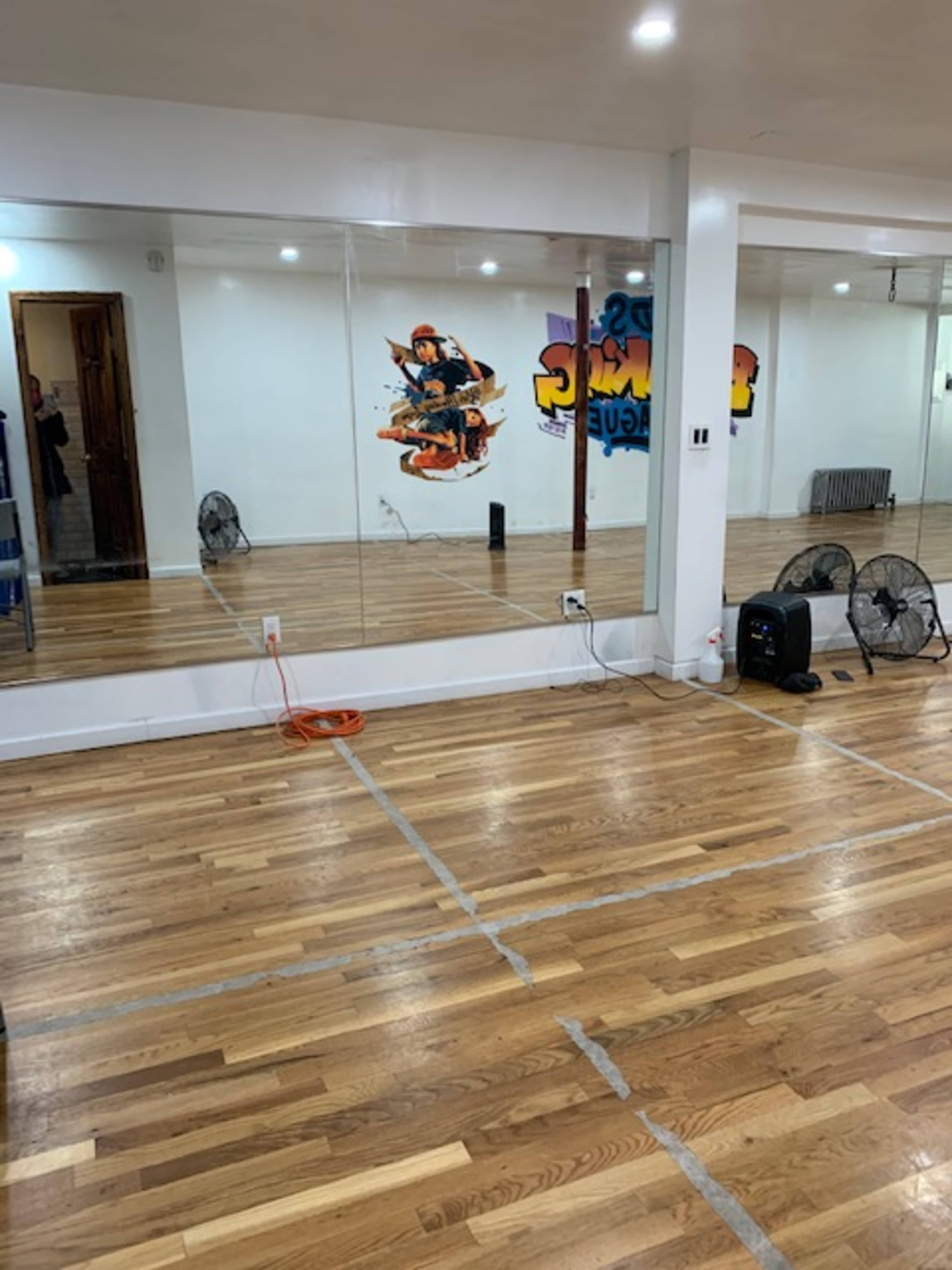 A dance studio with wooden flooring, large mirrors on one wall, and a mural featuring a character in the background.