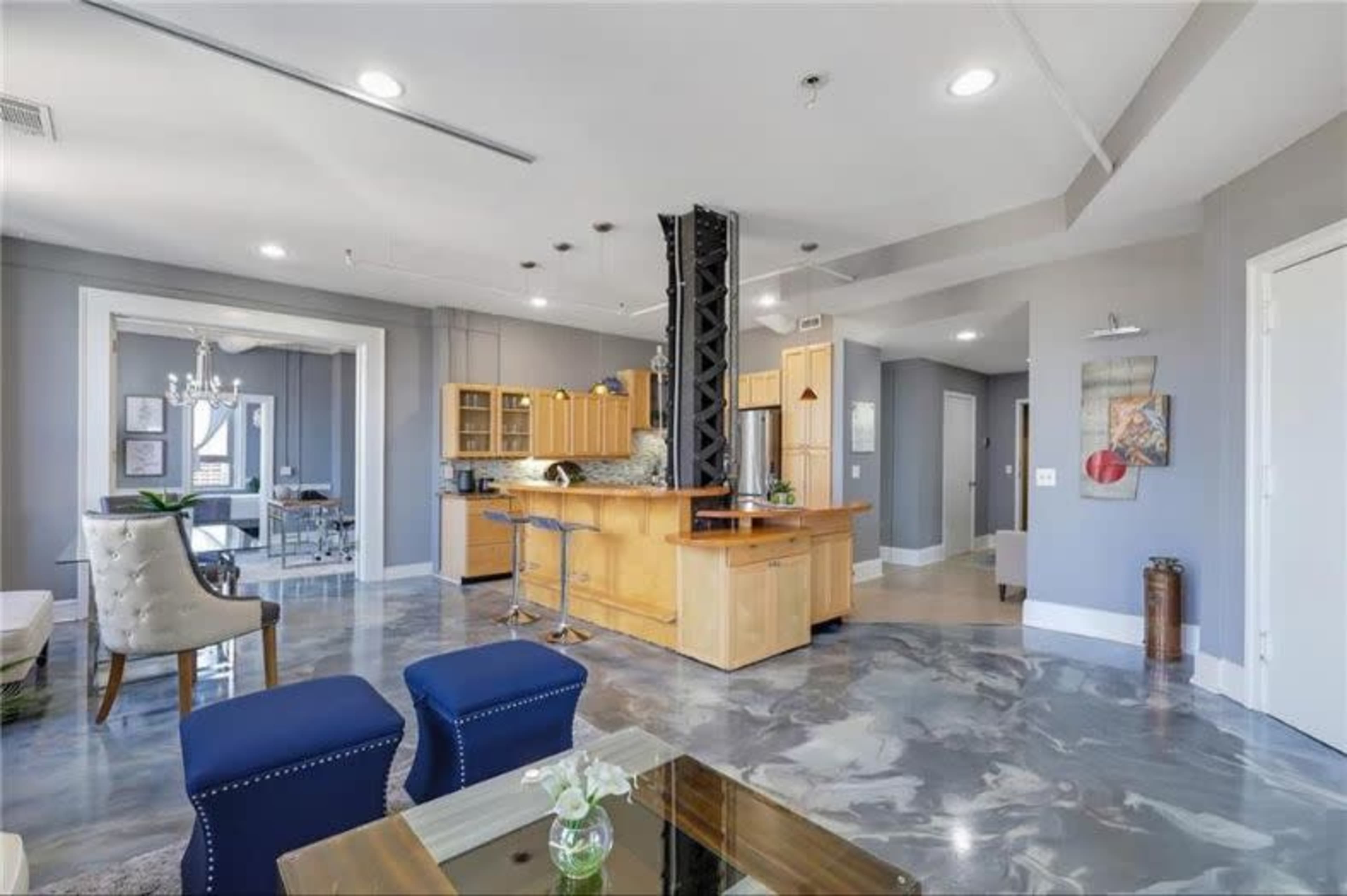 The image shows an open-concept living space featuring a kitchen with wooden cabinets, a central island, and polished concrete flooring.