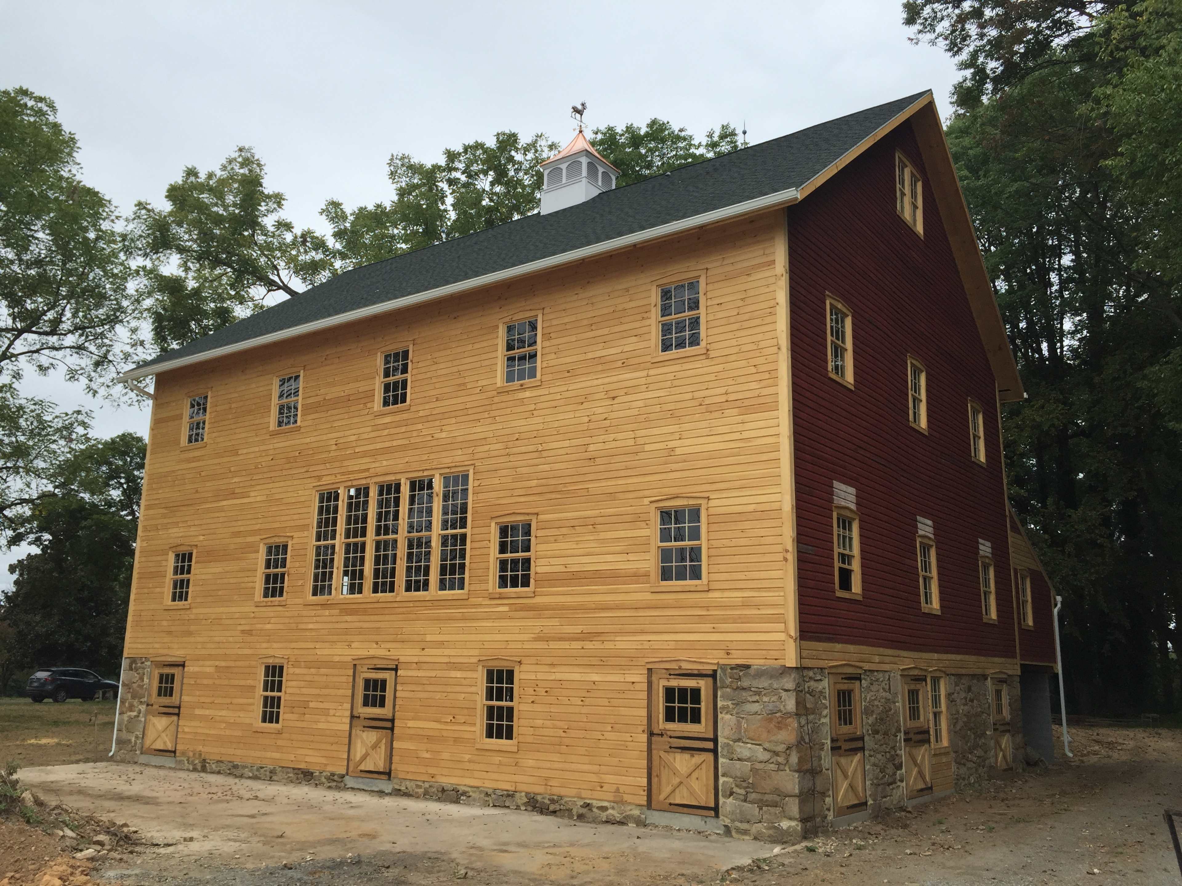 A large, two-tone wooden barn with a stone foundation and multiple windows on its side.