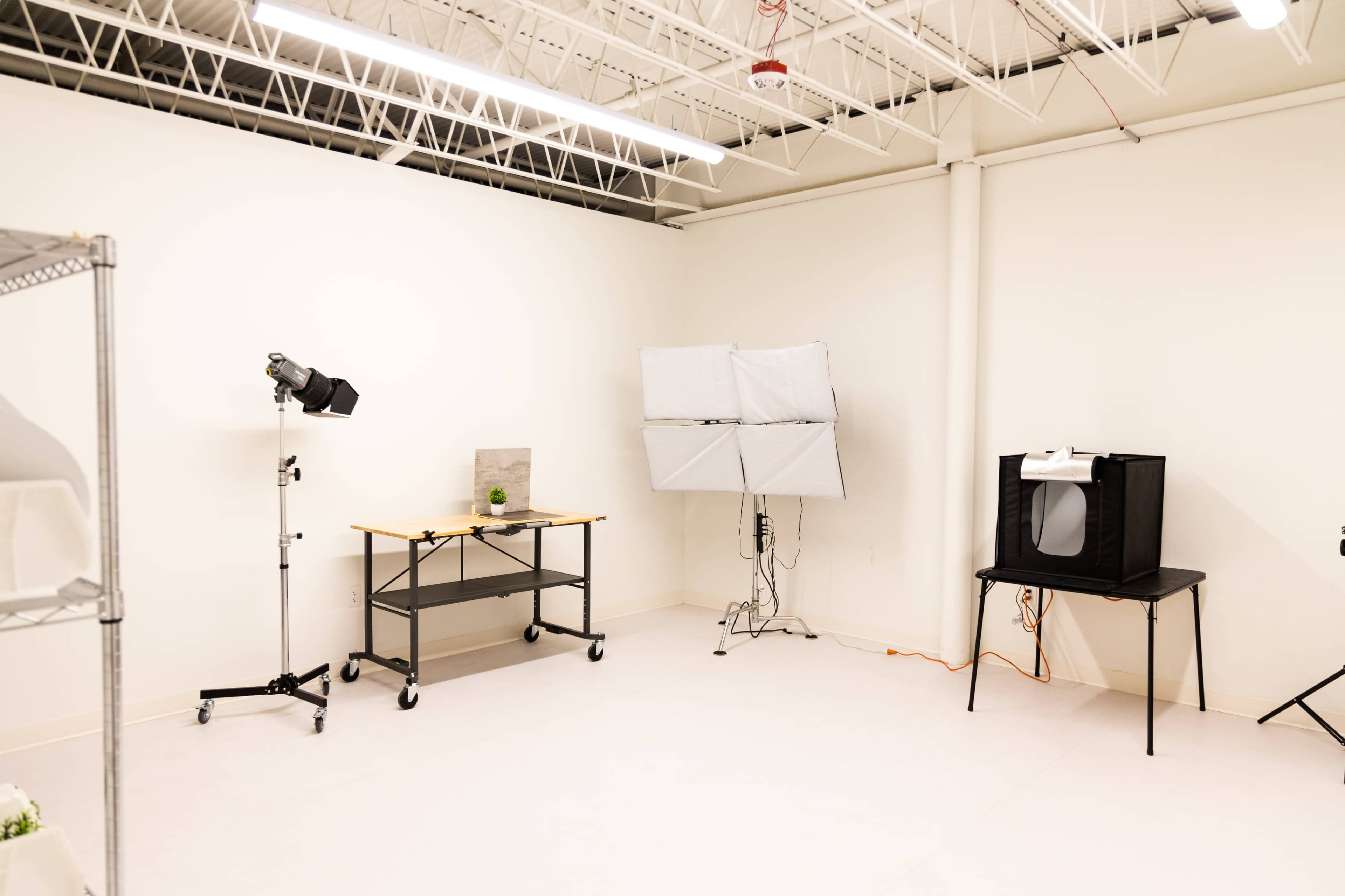 A minimalist photography studio with a table, softbox lighting, and a backdrop setup against a plain white wall.