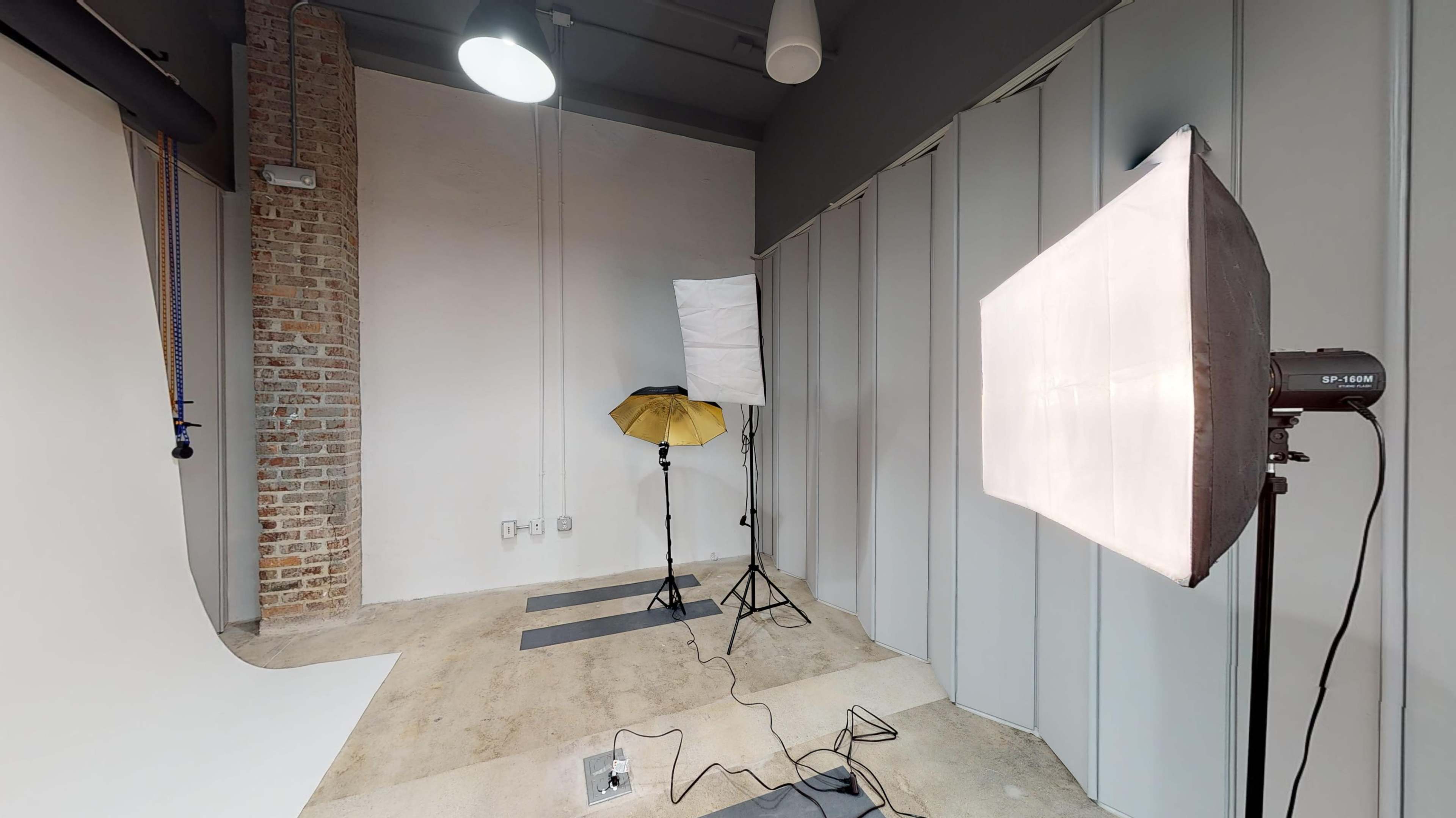 A photography studio with a gray backdrop, lighting equipment, and exposed brick walls.