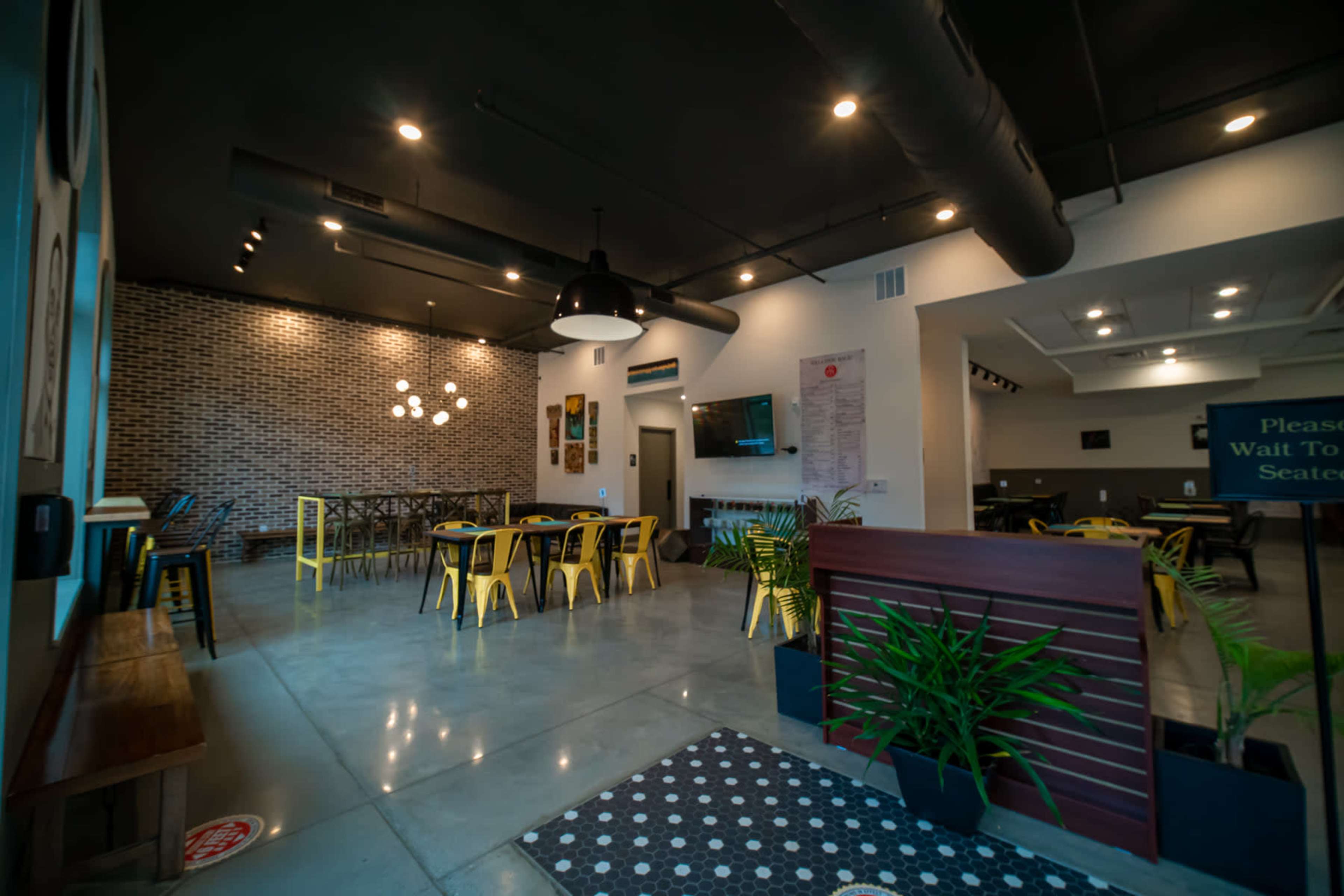 A modern café interior with yellow metal chairs and a mix of tables, featuring a brick wall and an open space for seating.