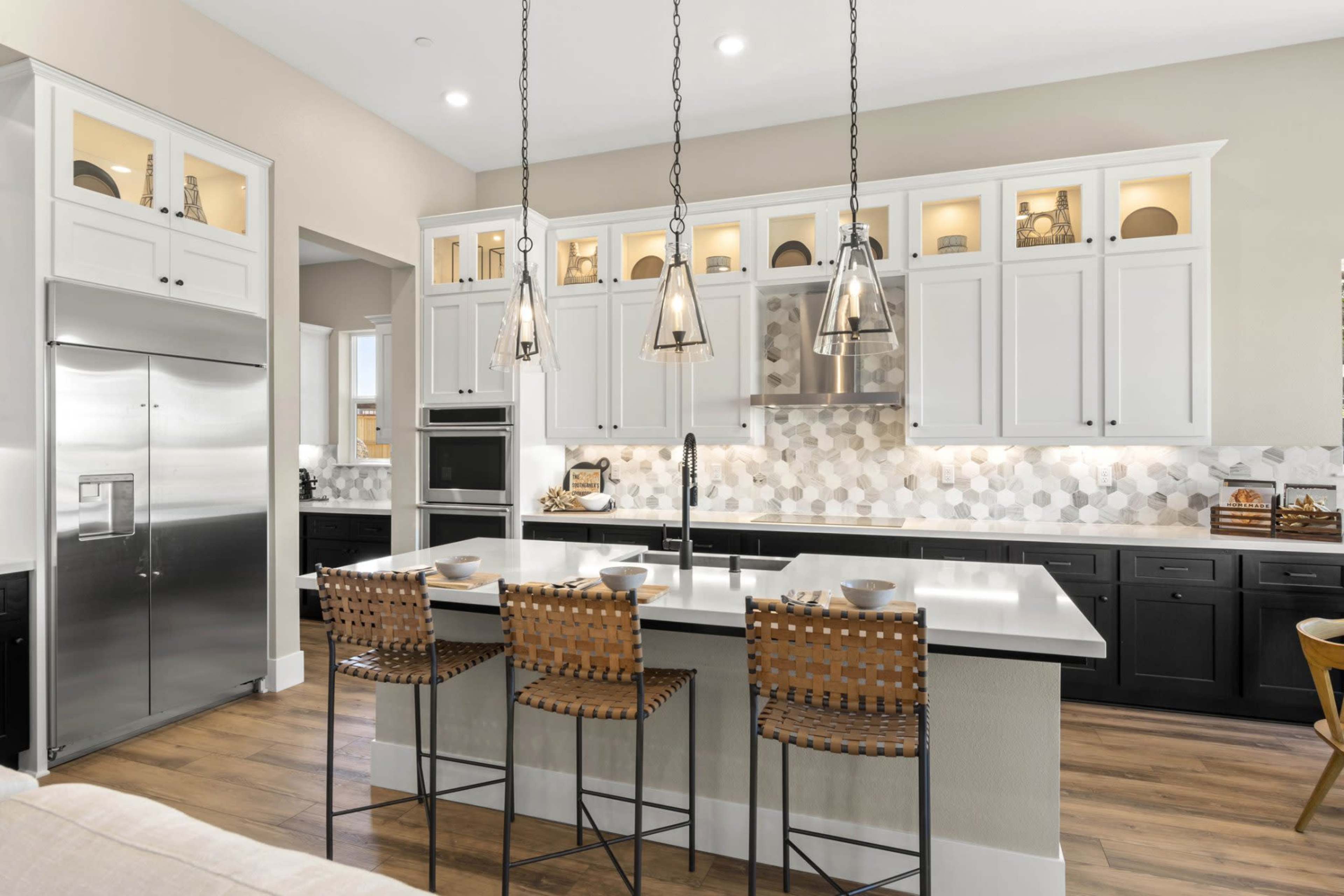 The image shows a modern kitchen featuring white cabinets, a gray island with bar stools, stainless steel appliances, and hexagonal tile backsplash.