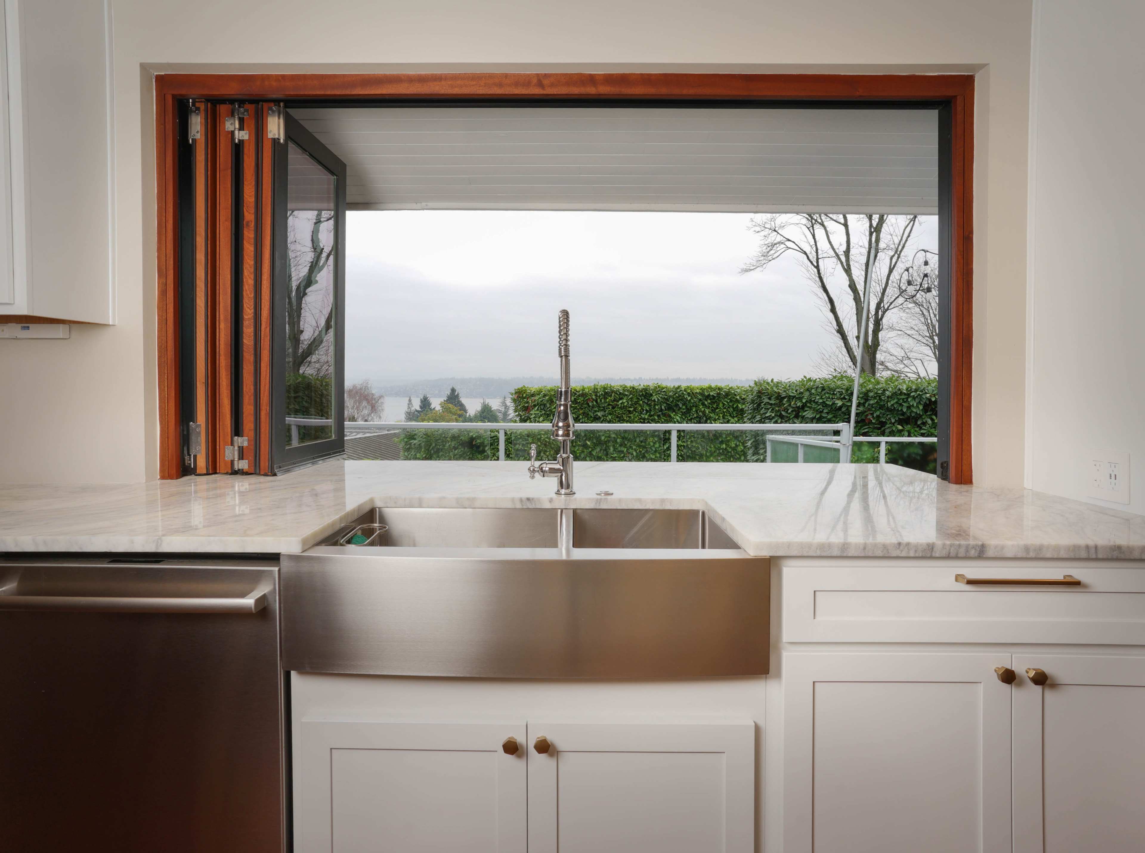 A kitchen with a farmhouse sink and large windows that open to a view of greenery outside.