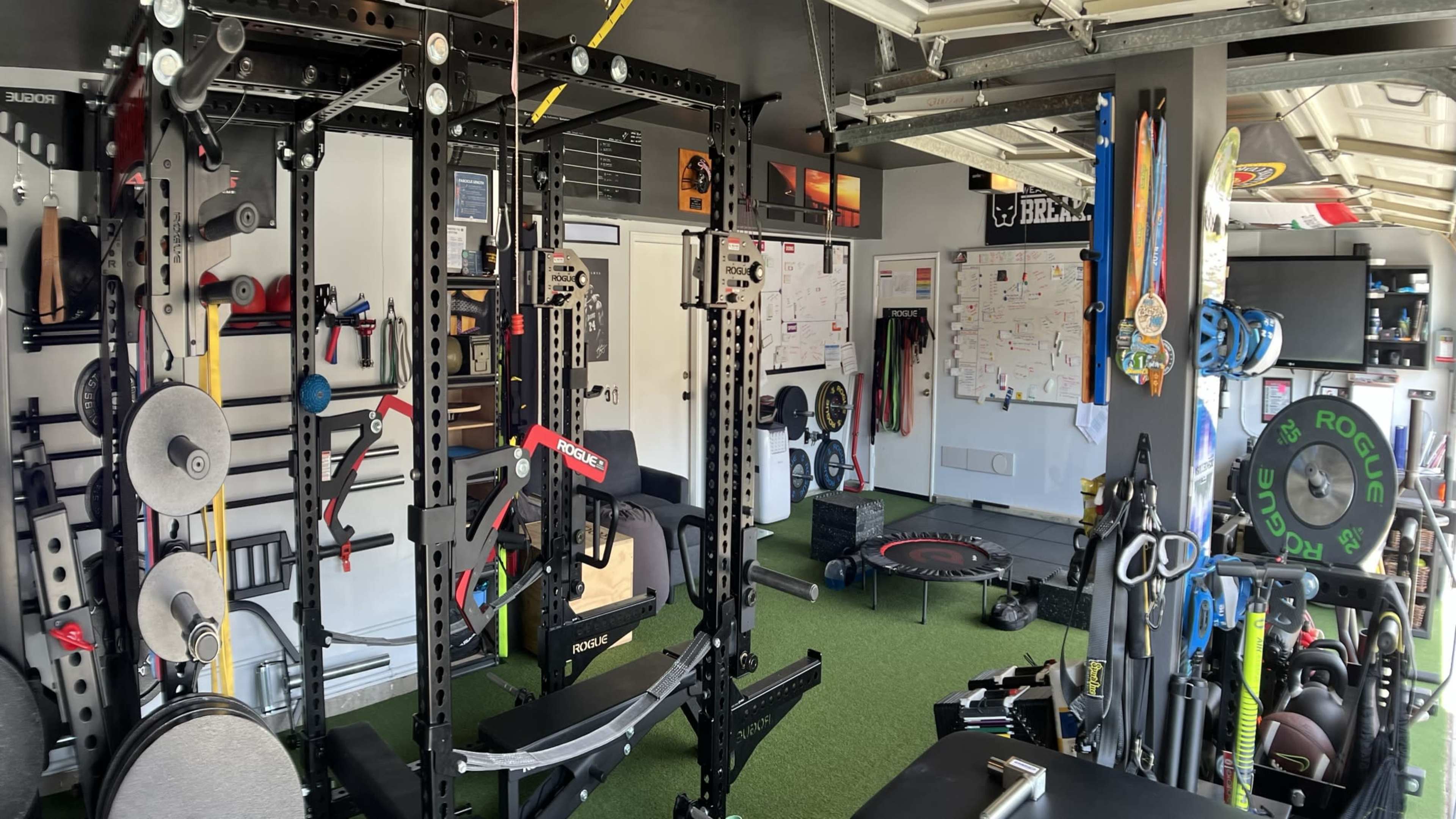 The image shows a well-equipped home gym with various exercise machines, weights, and fitness accessories arranged neatly in a garage.