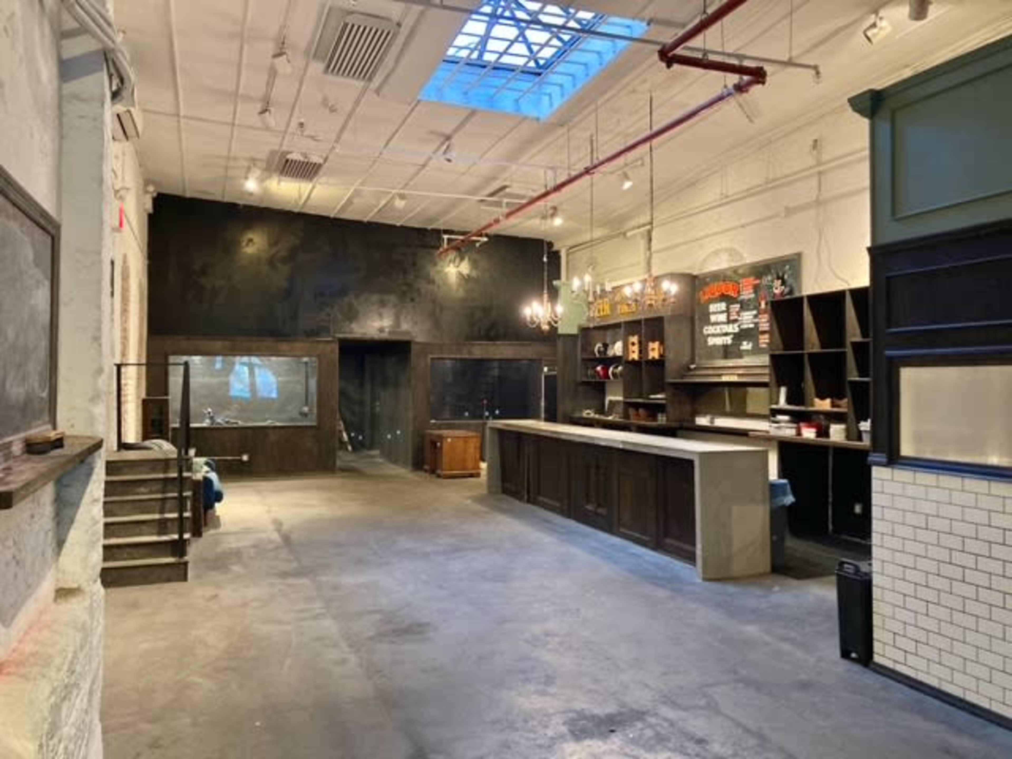 The image shows an empty interior space with a bar area, dark walls, industrial lighting, and a skylight, set up for a possible commercial use.