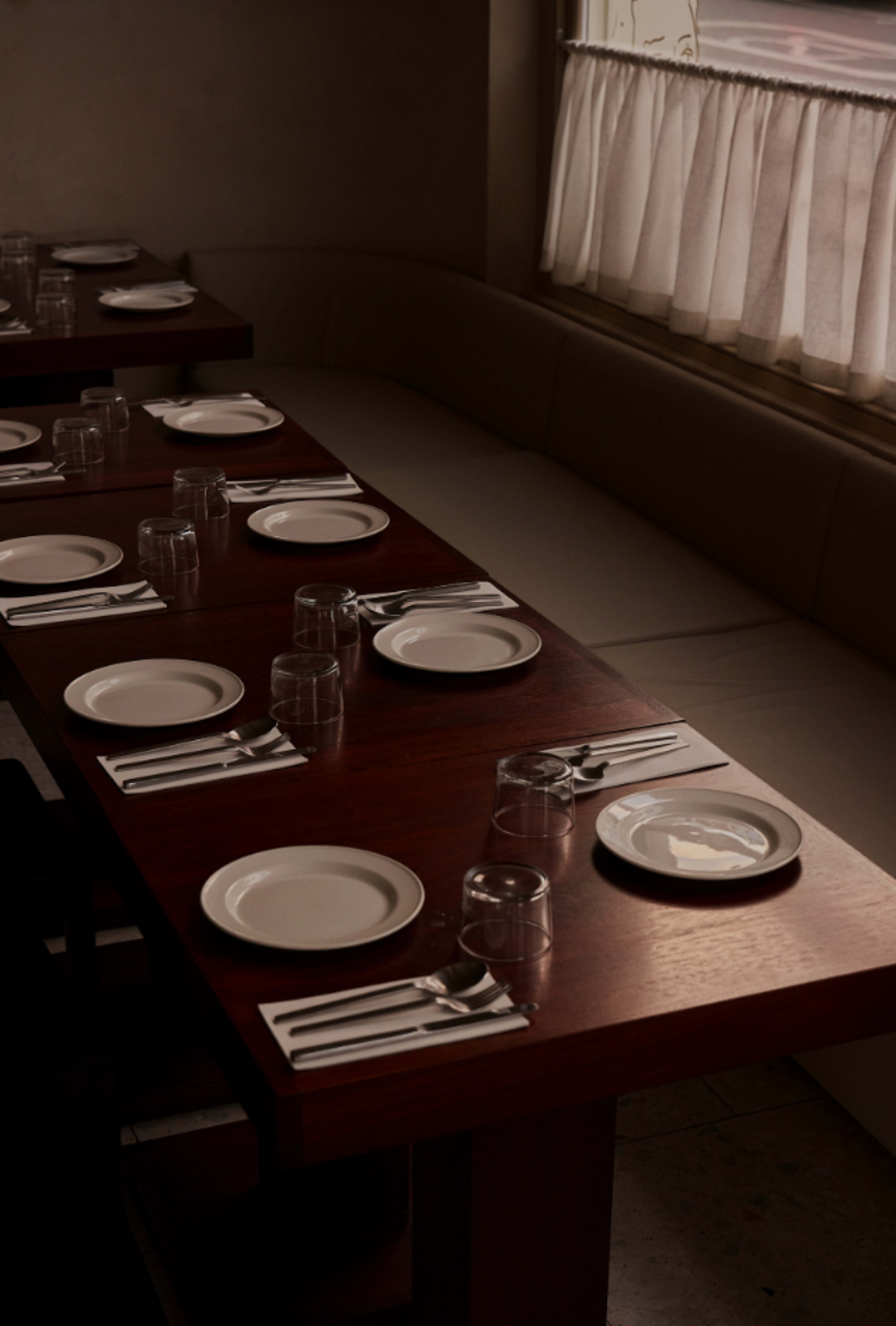A long wooden table is set with white plates, glassware, and cutlery, ready for a meal.