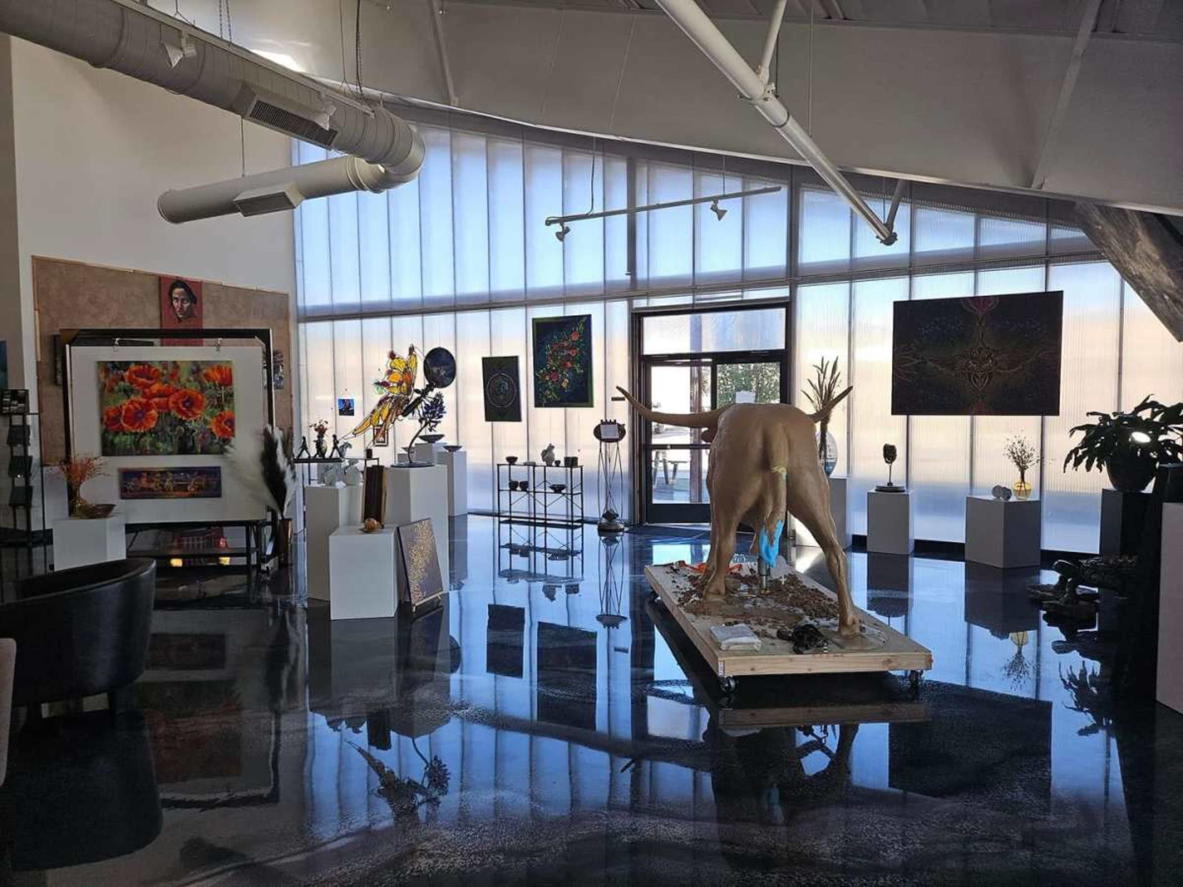The scene features an art gallery with various artworks displayed on the walls and stands, including a large sculpture of a deer in the center.