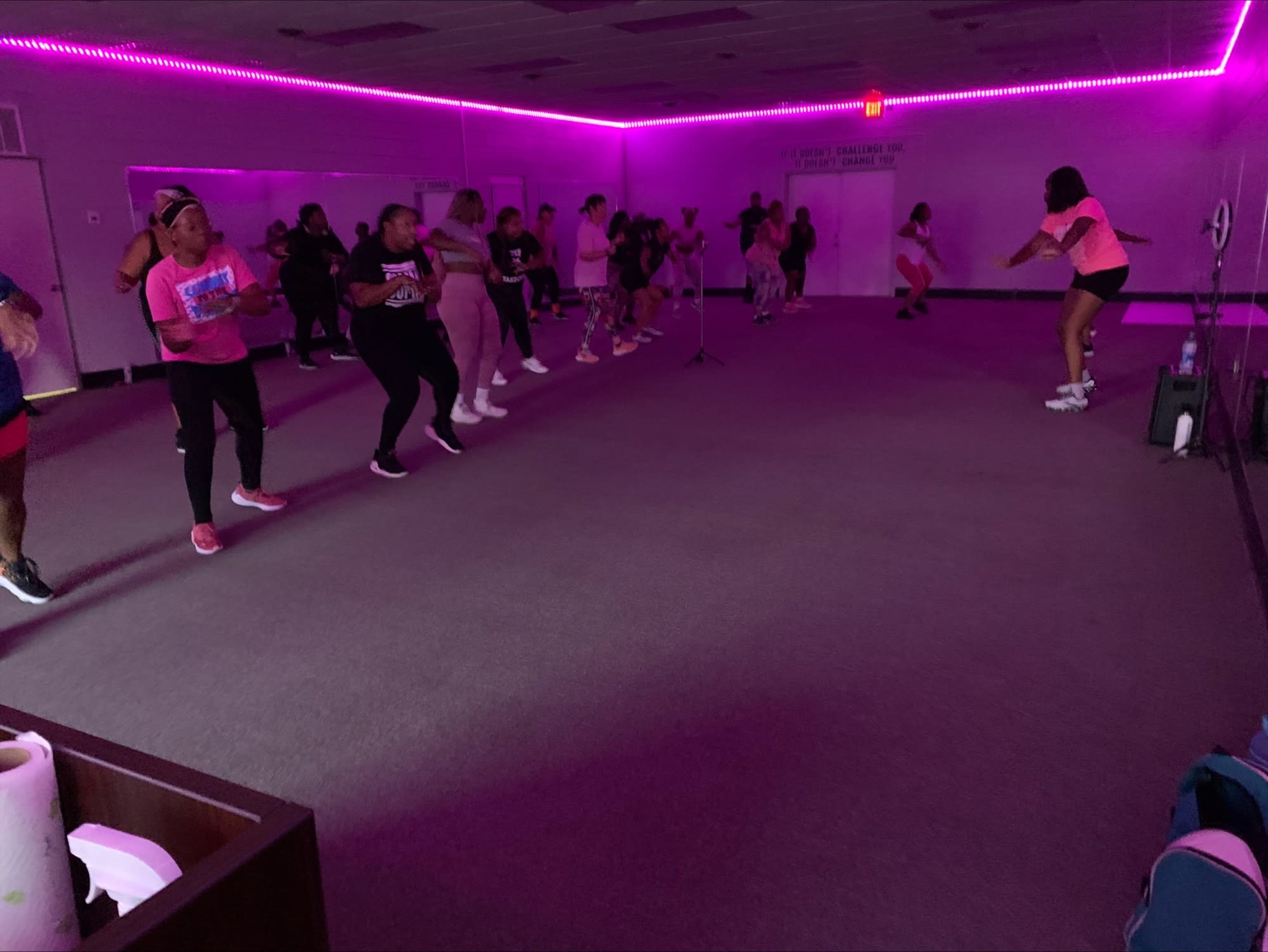 A group of people are participating in an exercise class in a room lit with purple lights.