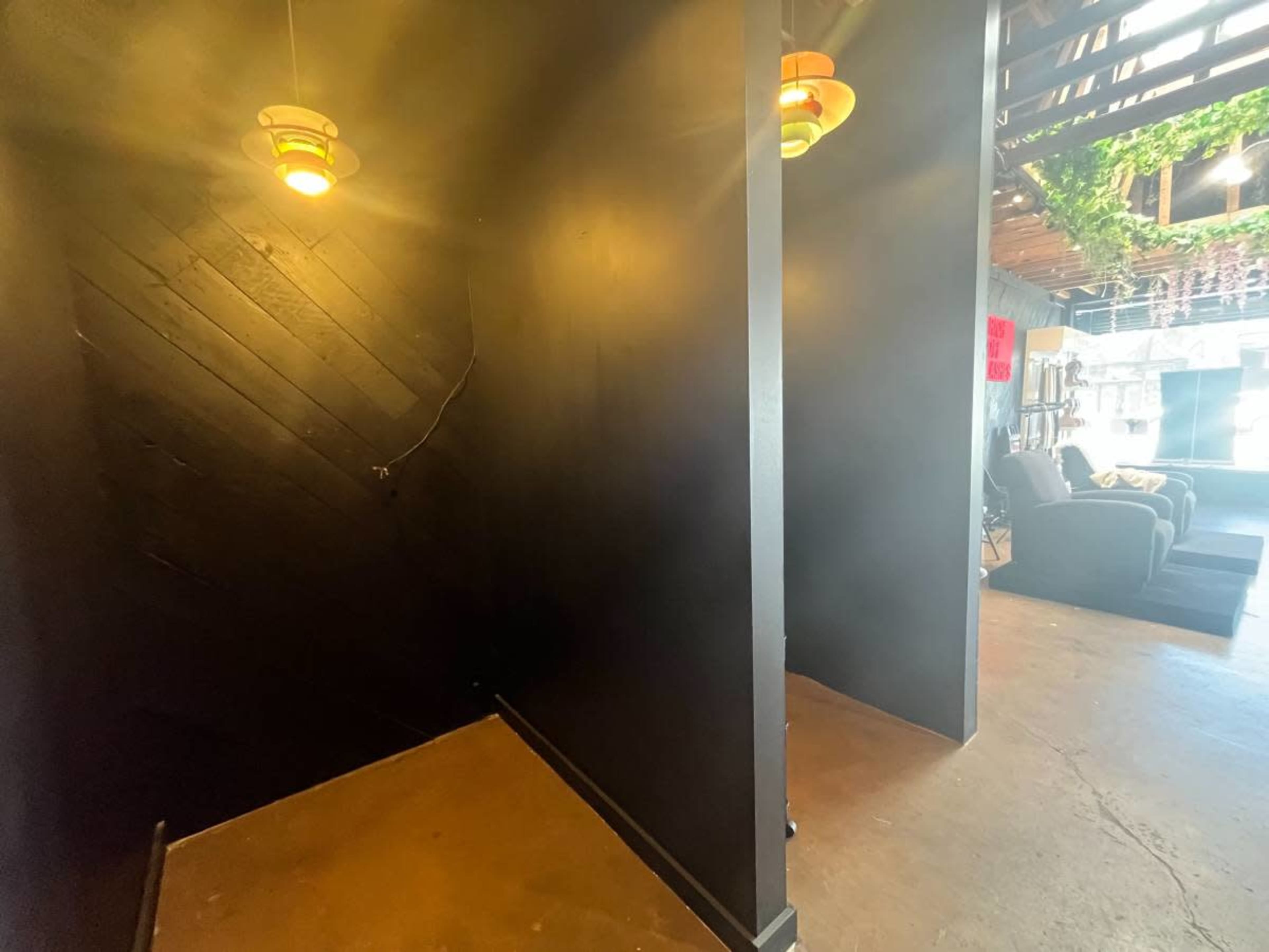 The image shows a dimly lit corner of an interior space with black walls, a concrete floor, and hanging light fixtures.