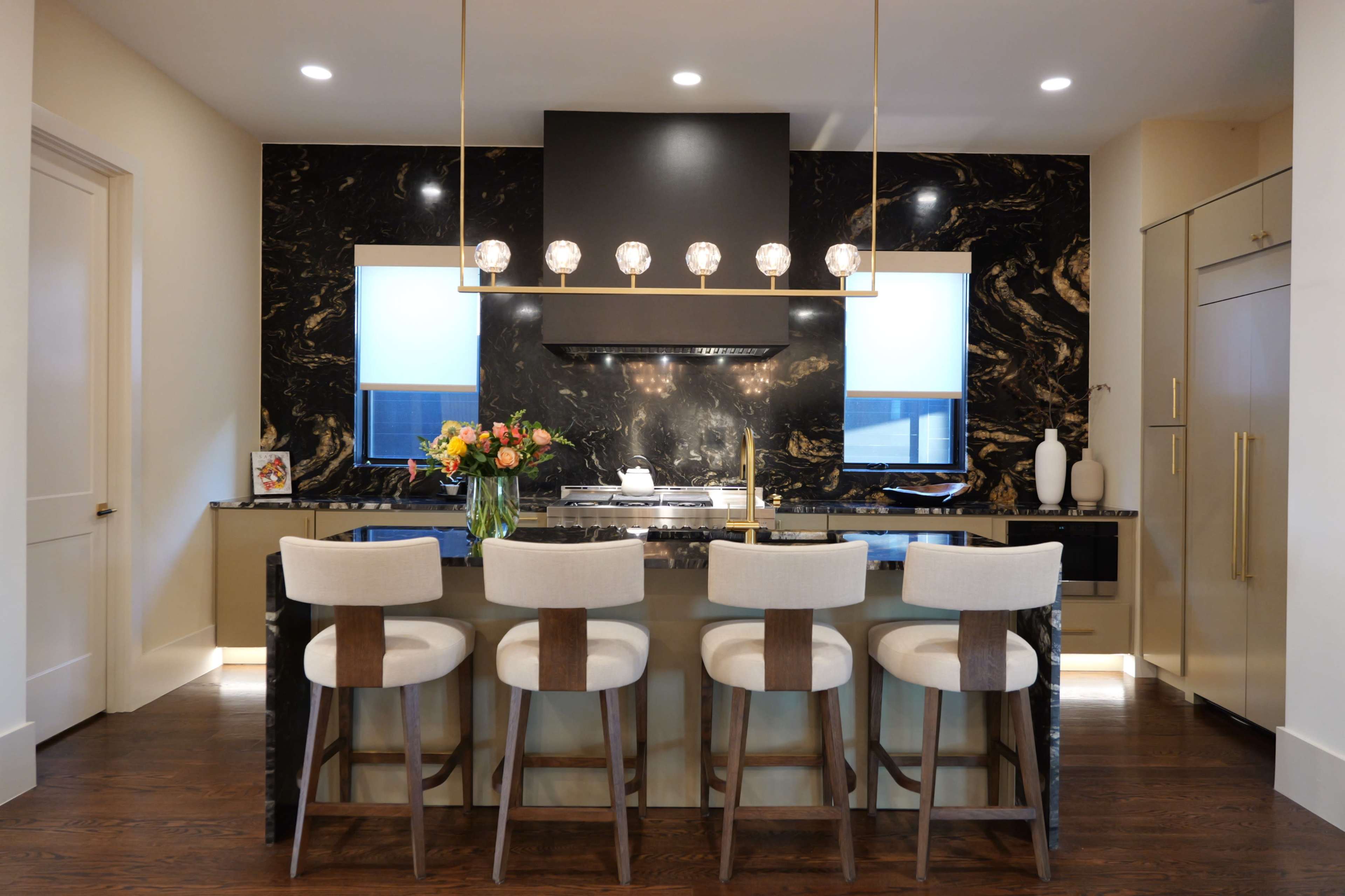 The kitchen features black marble countertops, modern pendant lighting, and four stools arranged around a central island.