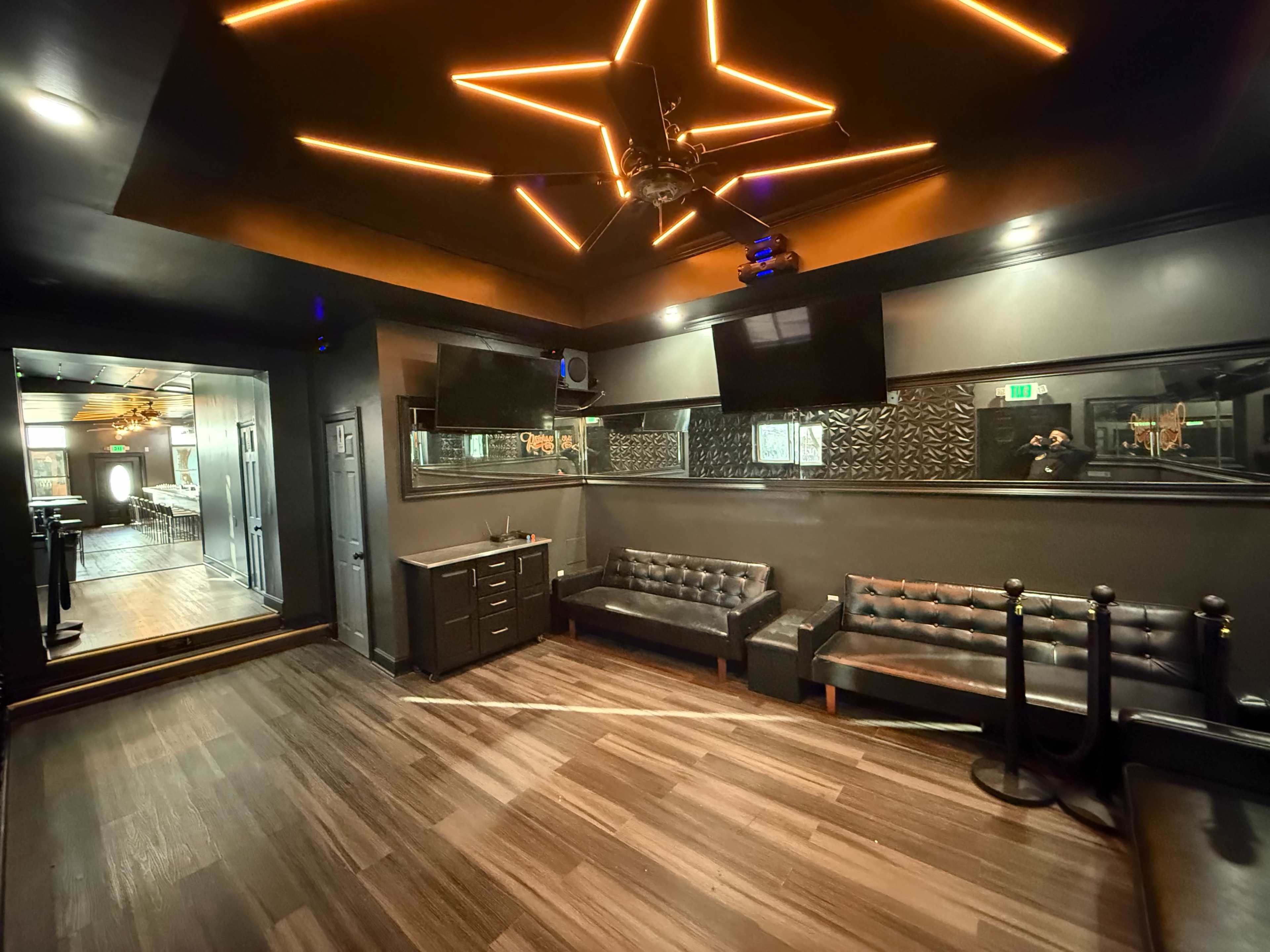 The image shows a modern lounge area featuring dark walls, leather couches, and a ceiling with star-shaped lighting.