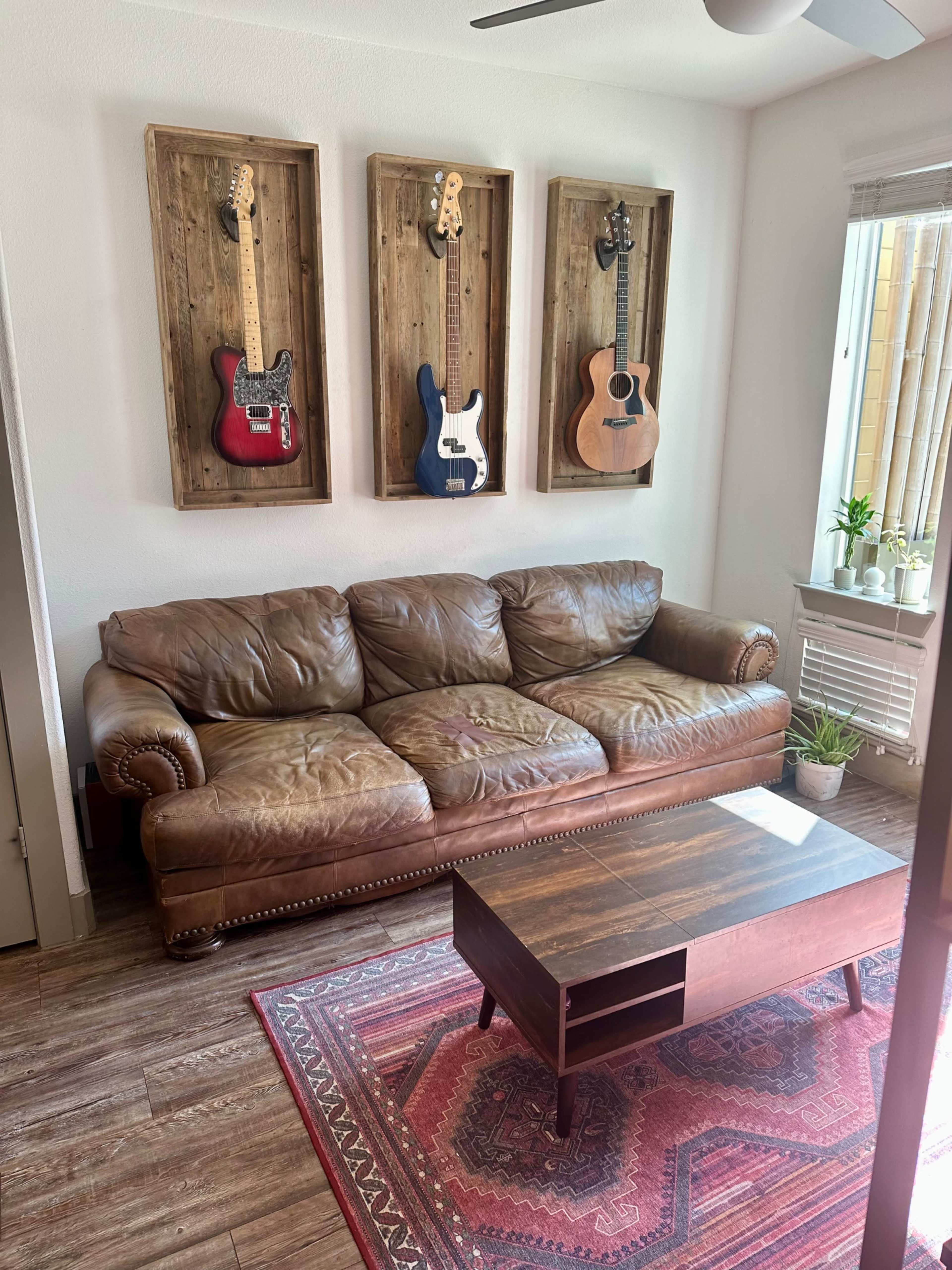 The image features a living room with a brown leather sofa, a wooden coffee table, and three framed guitars mounted on the wall.