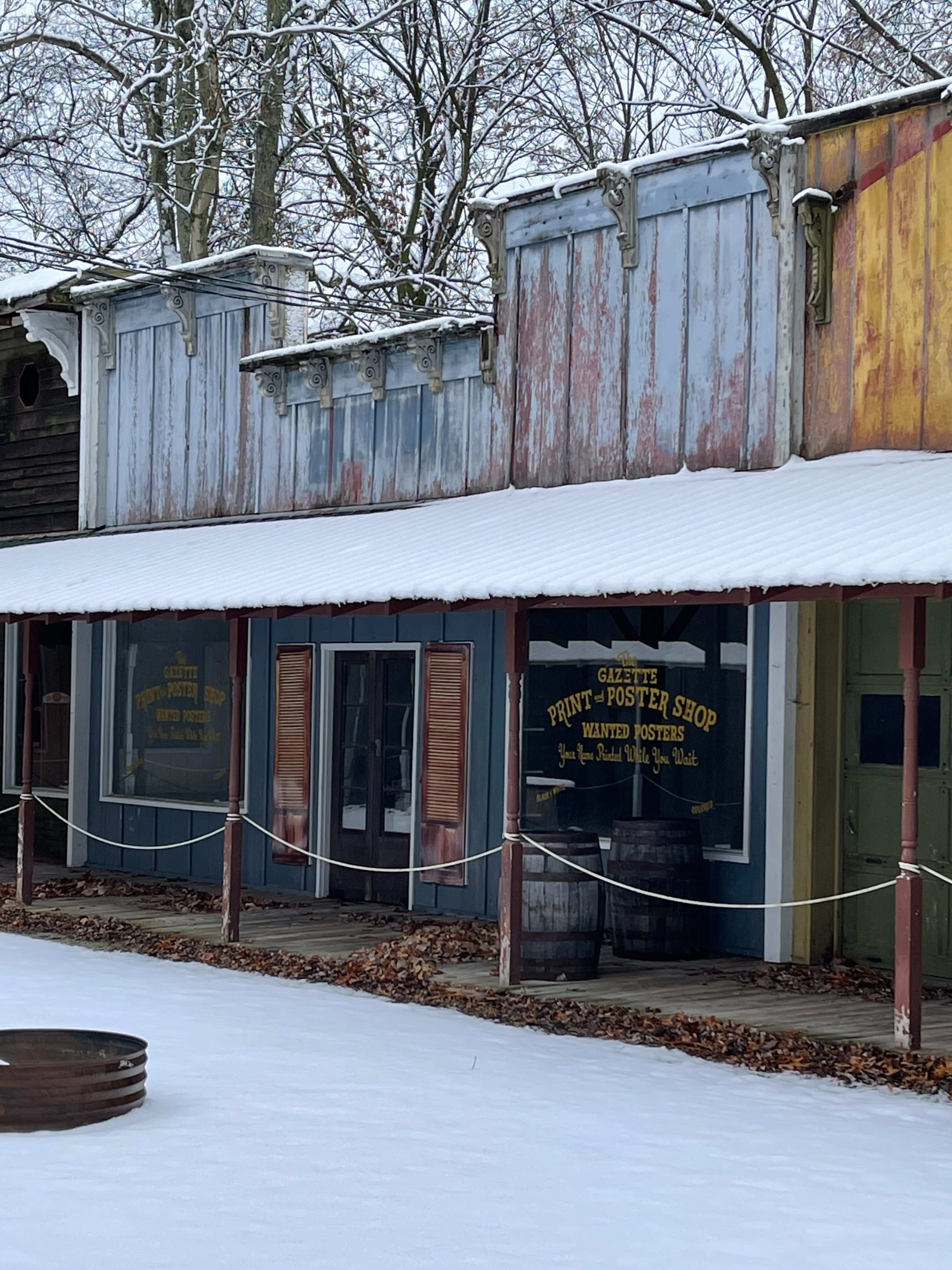 A row of old wooden buildings with a sign for a print and poster shop, covered in snow.