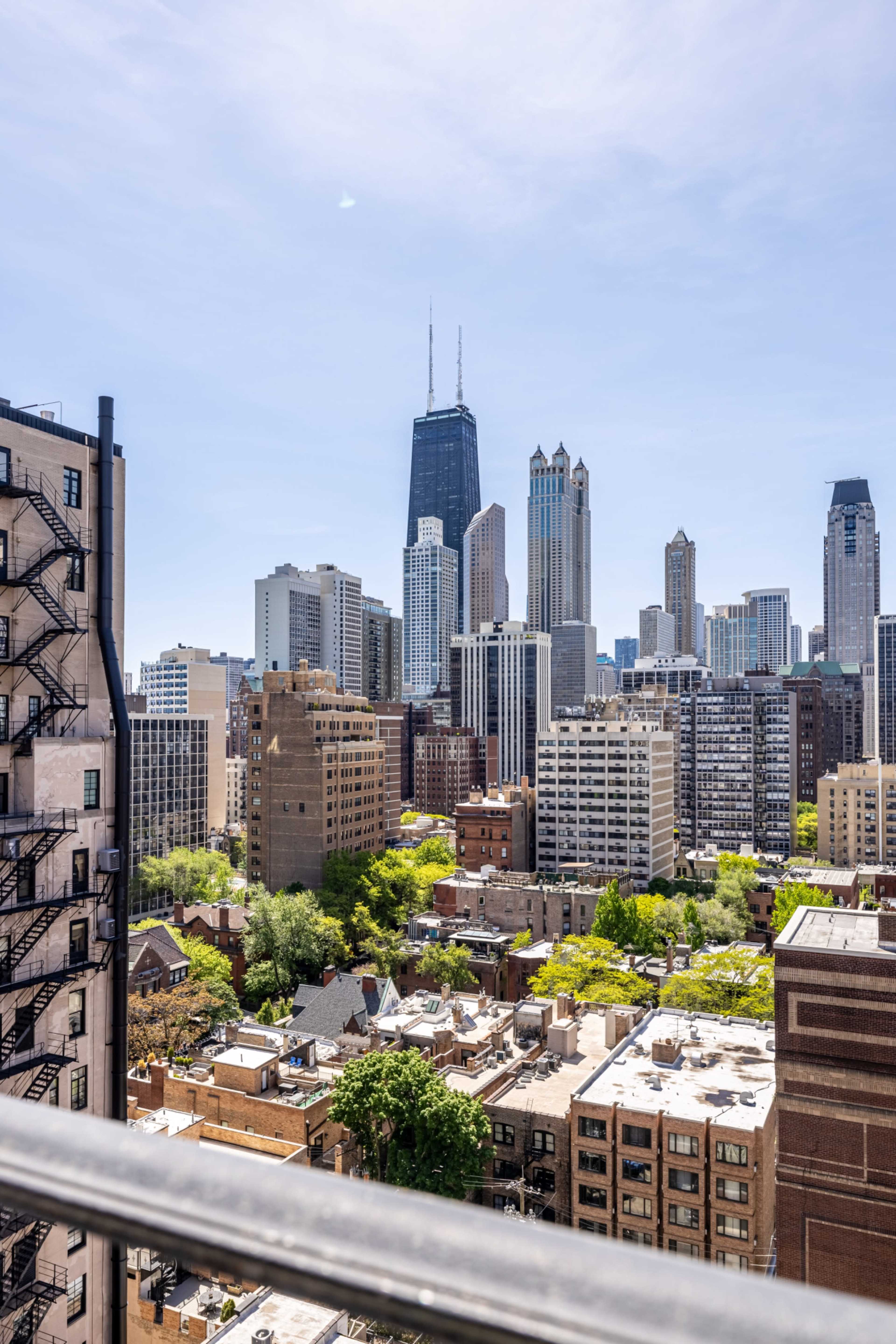 The image shows a view of a city skyline featuring tall buildings, including the Willis Tower, framed by residential structures and greenery in the foreground.
