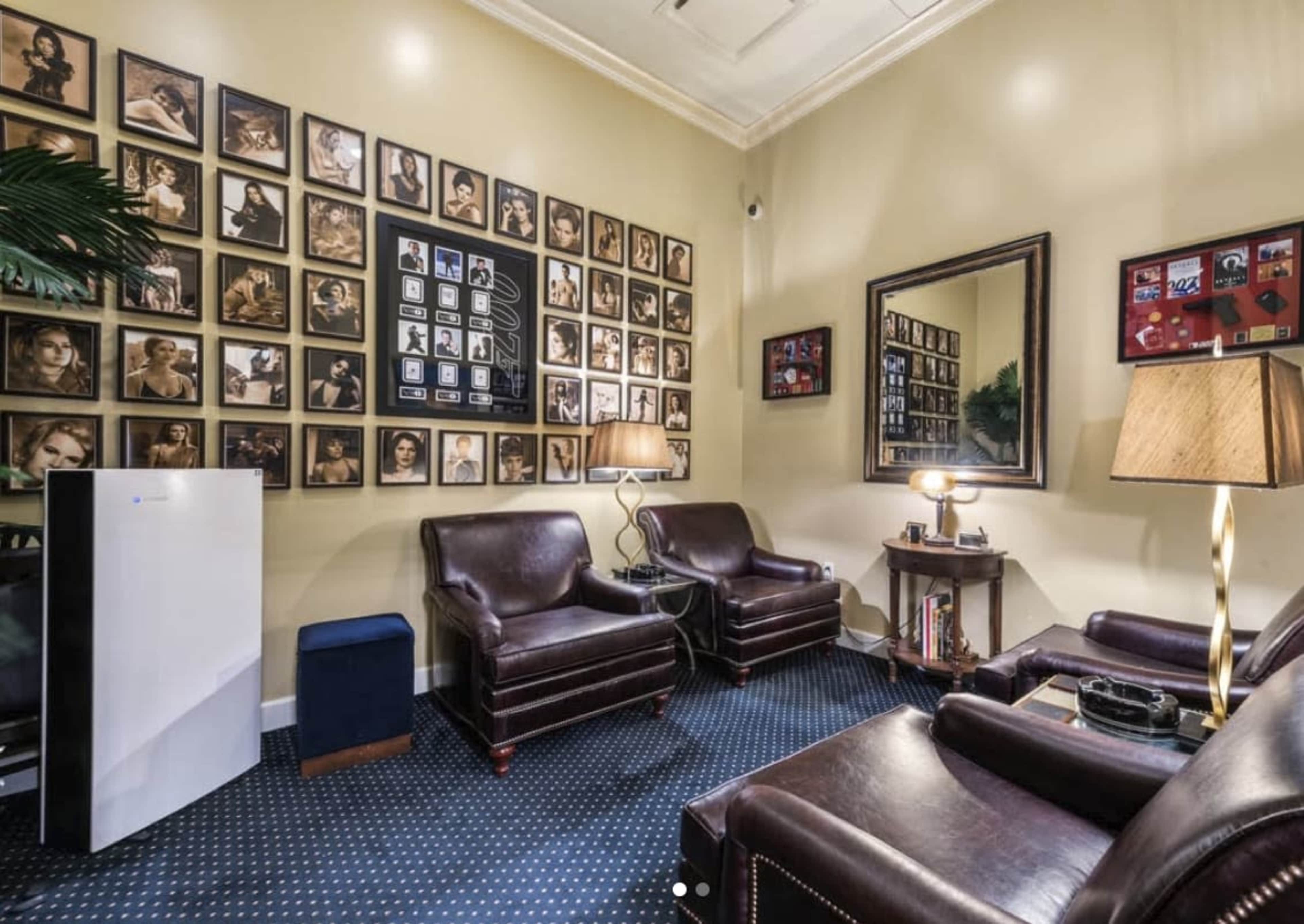 The image shows a well-decorated room with two leather chairs, a decorative mirror, and a wall filled with framed photographs.