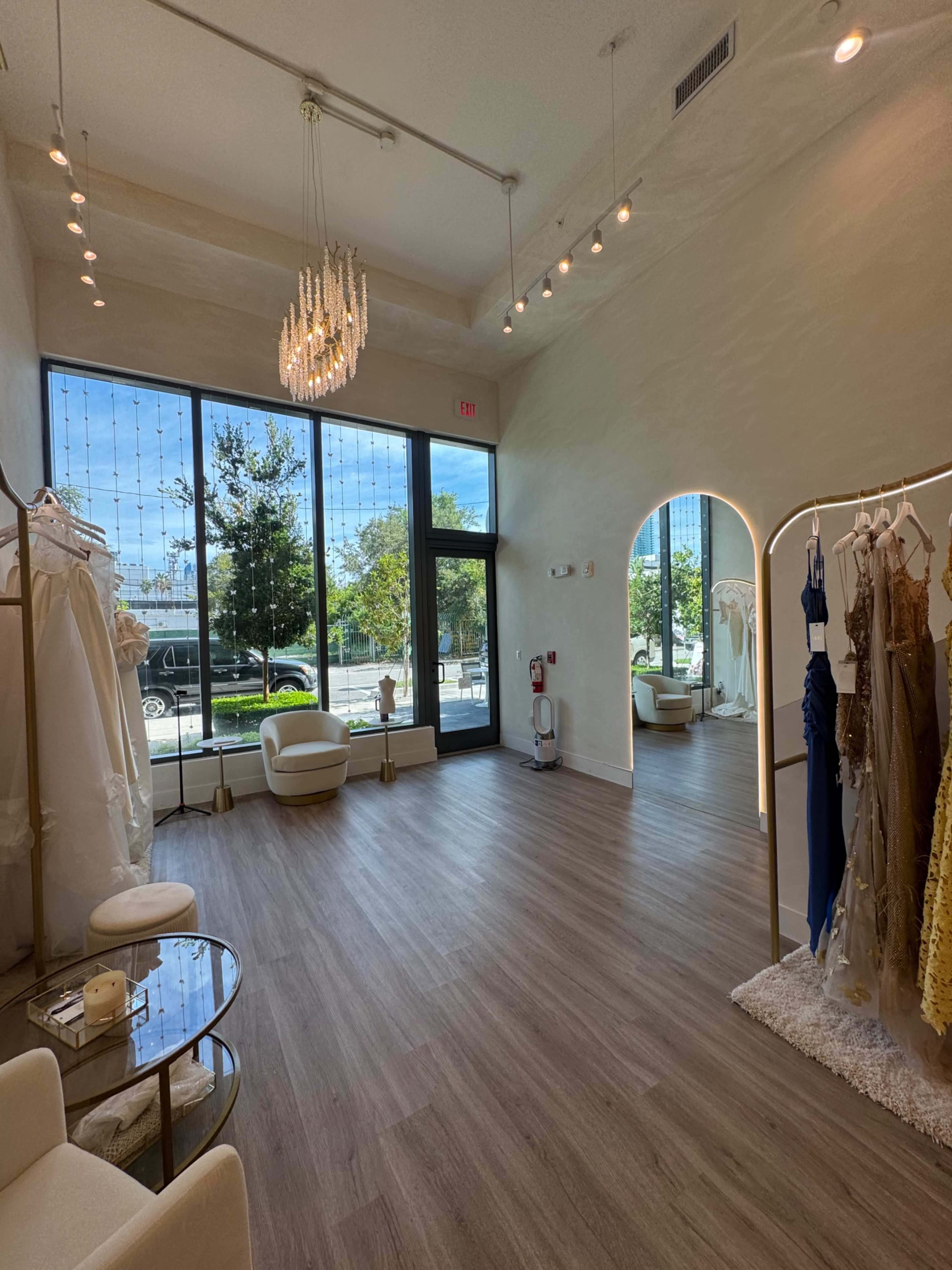 A bright bridal shop features elegant gowns displayed on racks, large windows allowing natural light in, and a modern seating area.