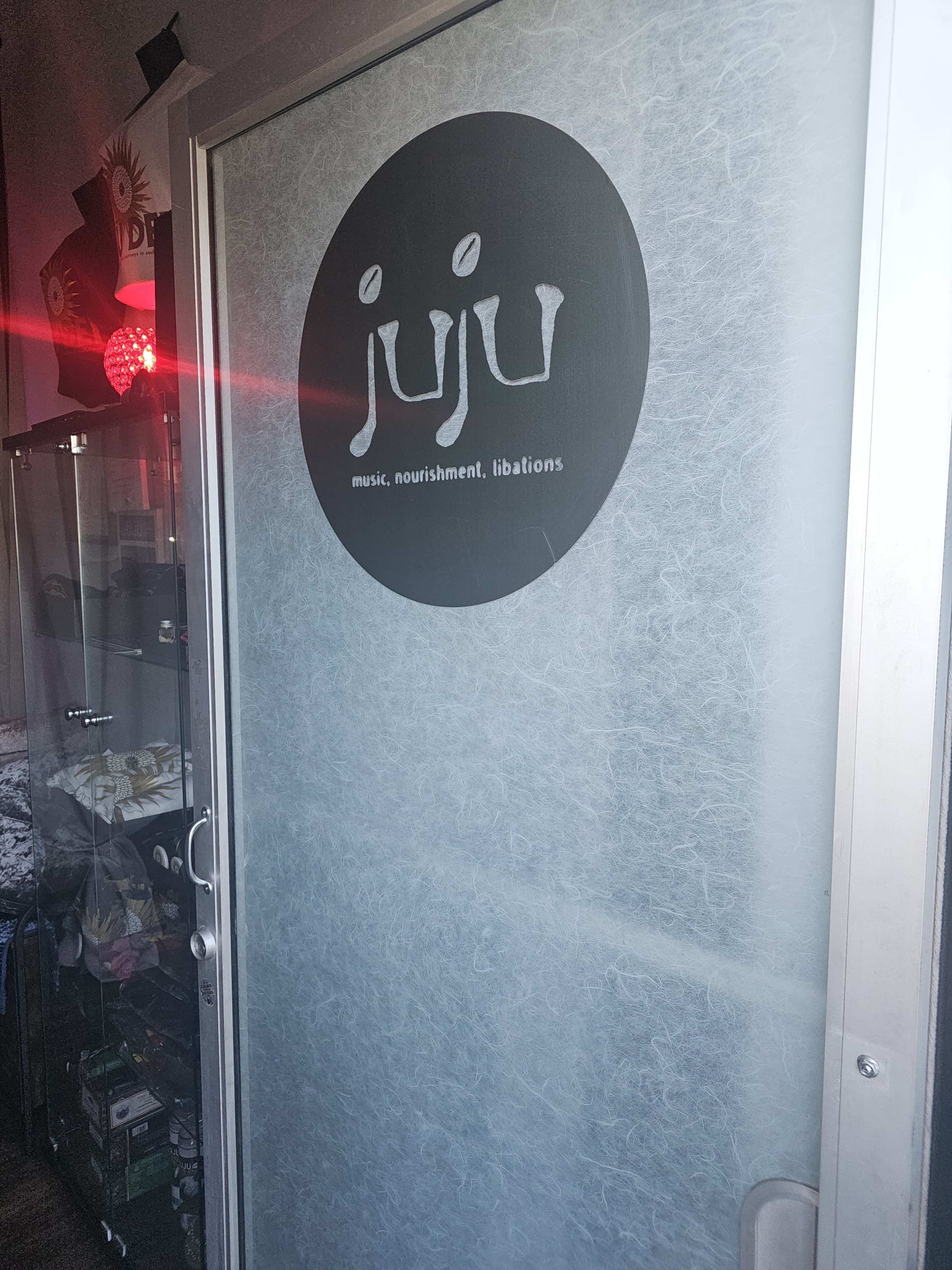 A frosted glass door with a circular logo that reads "juju music, nourishment, libations."