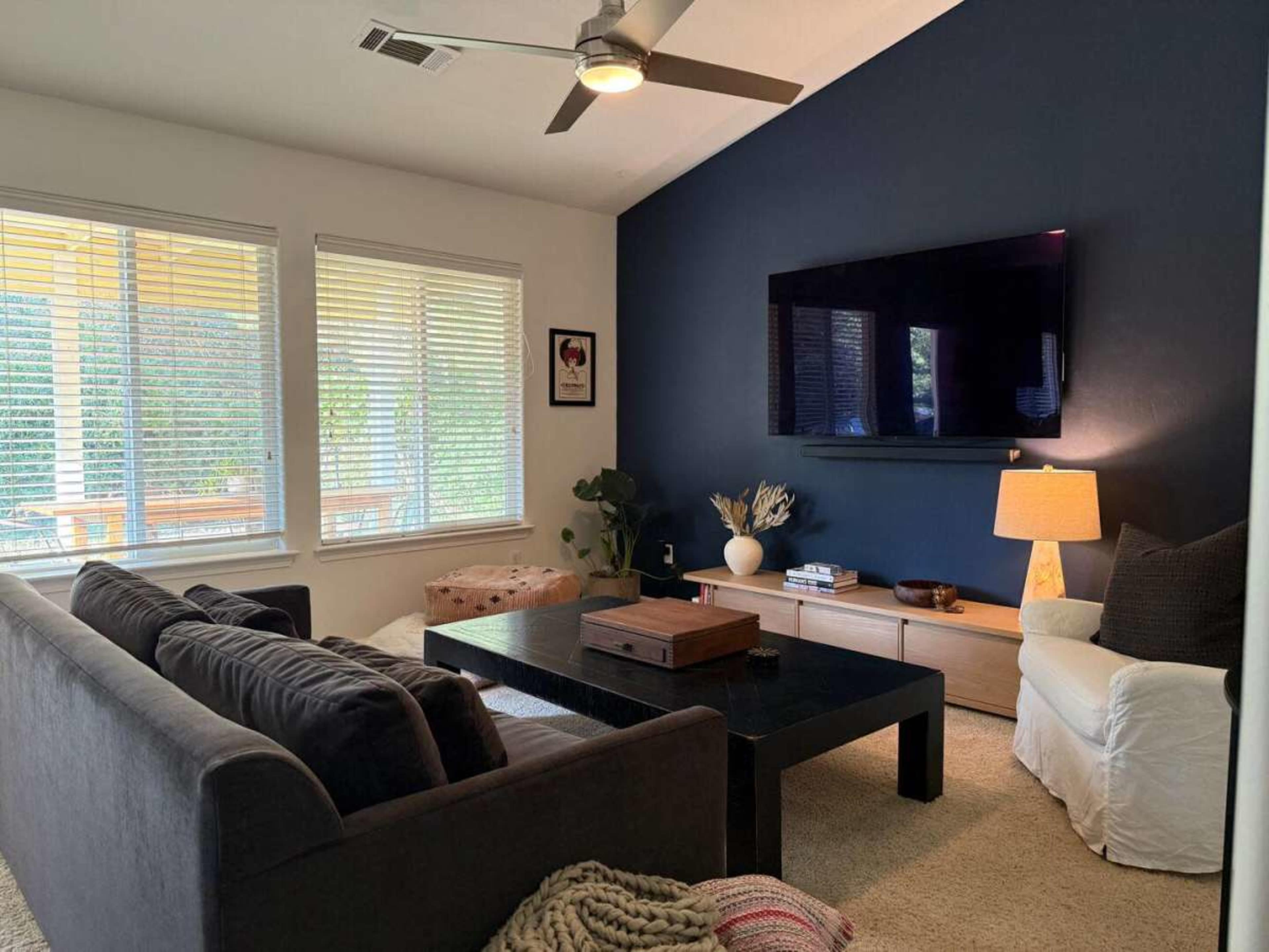 The image shows a modern living room featuring a dark accent wall, a television mounted above a light-colored media console, and comfortable seating arranged around a black coffee table.