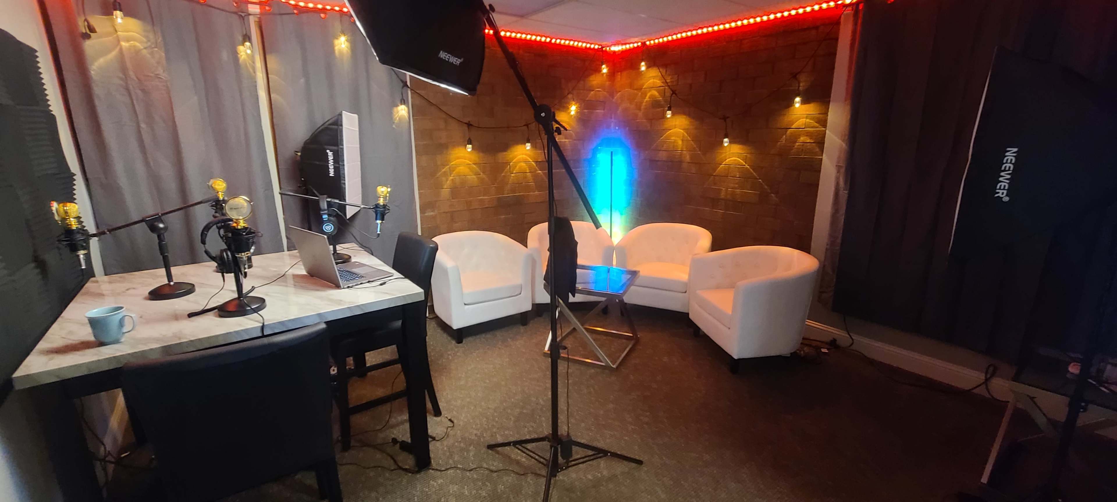 A recording studio with a table, chairs, microphones, and ambient lighting.