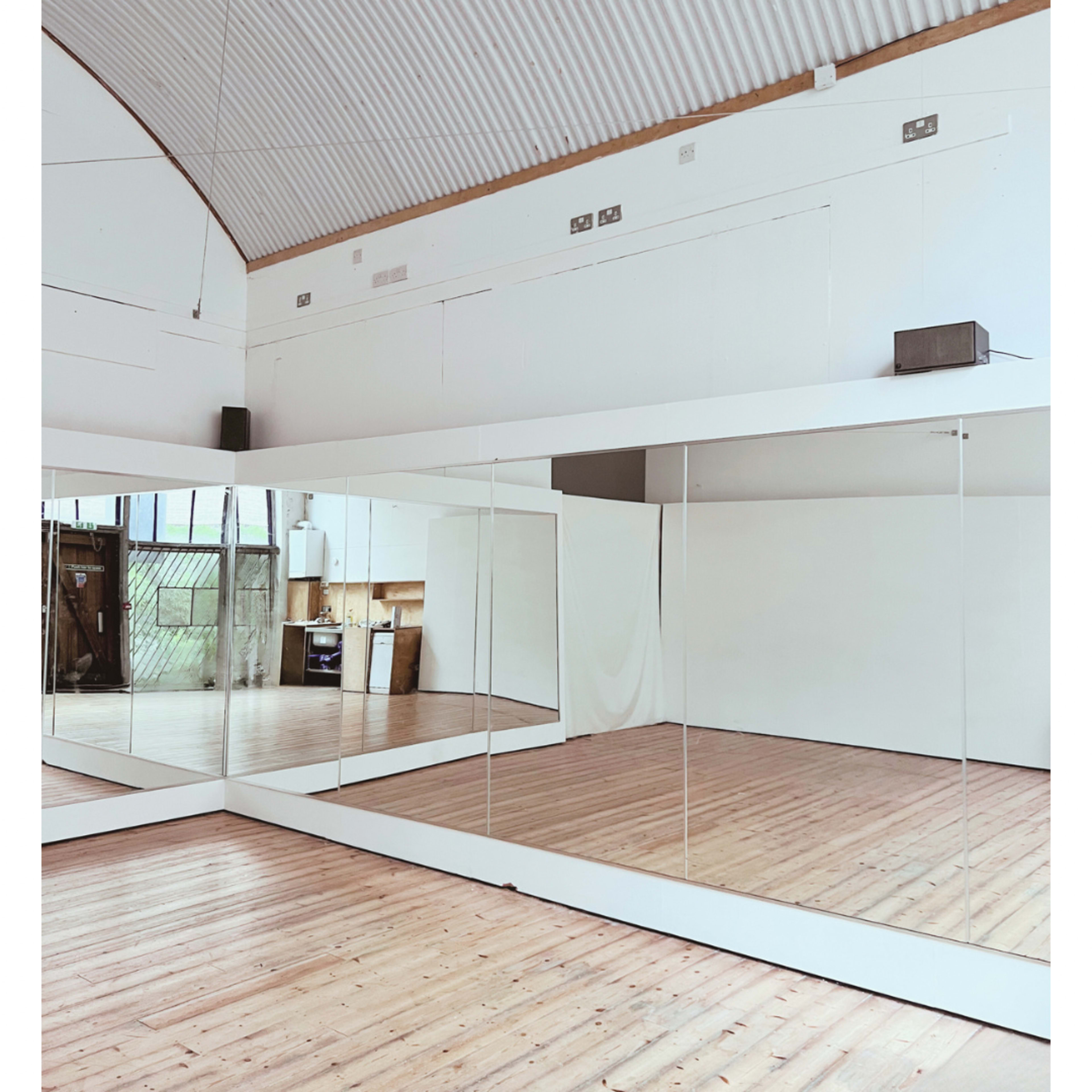 A spacious room with wooden flooring and large mirrors along one wall, complemented by white walls and a high ceiling.