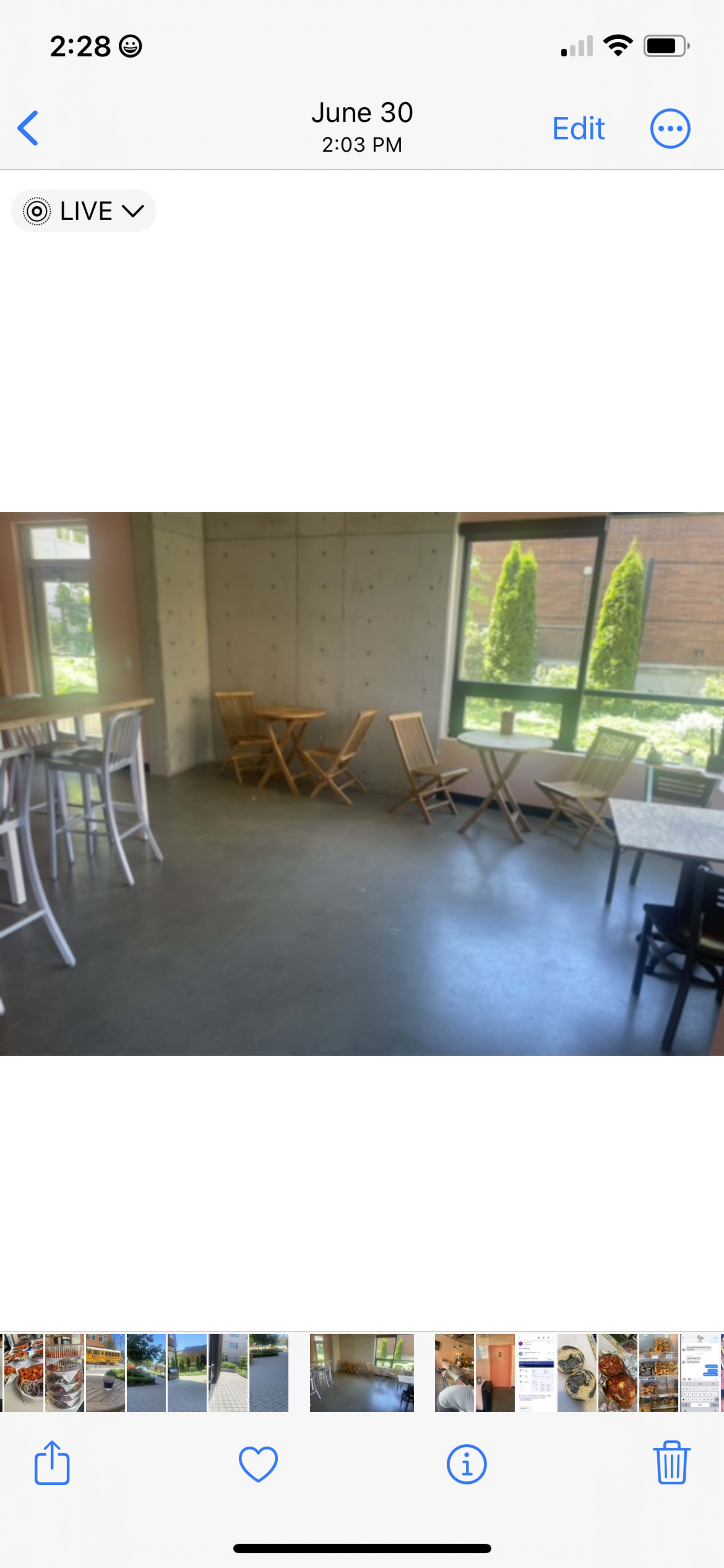 The image shows a modern cafe interior with a concrete wall, wooden tables, and several empty chairs positioned around the space.