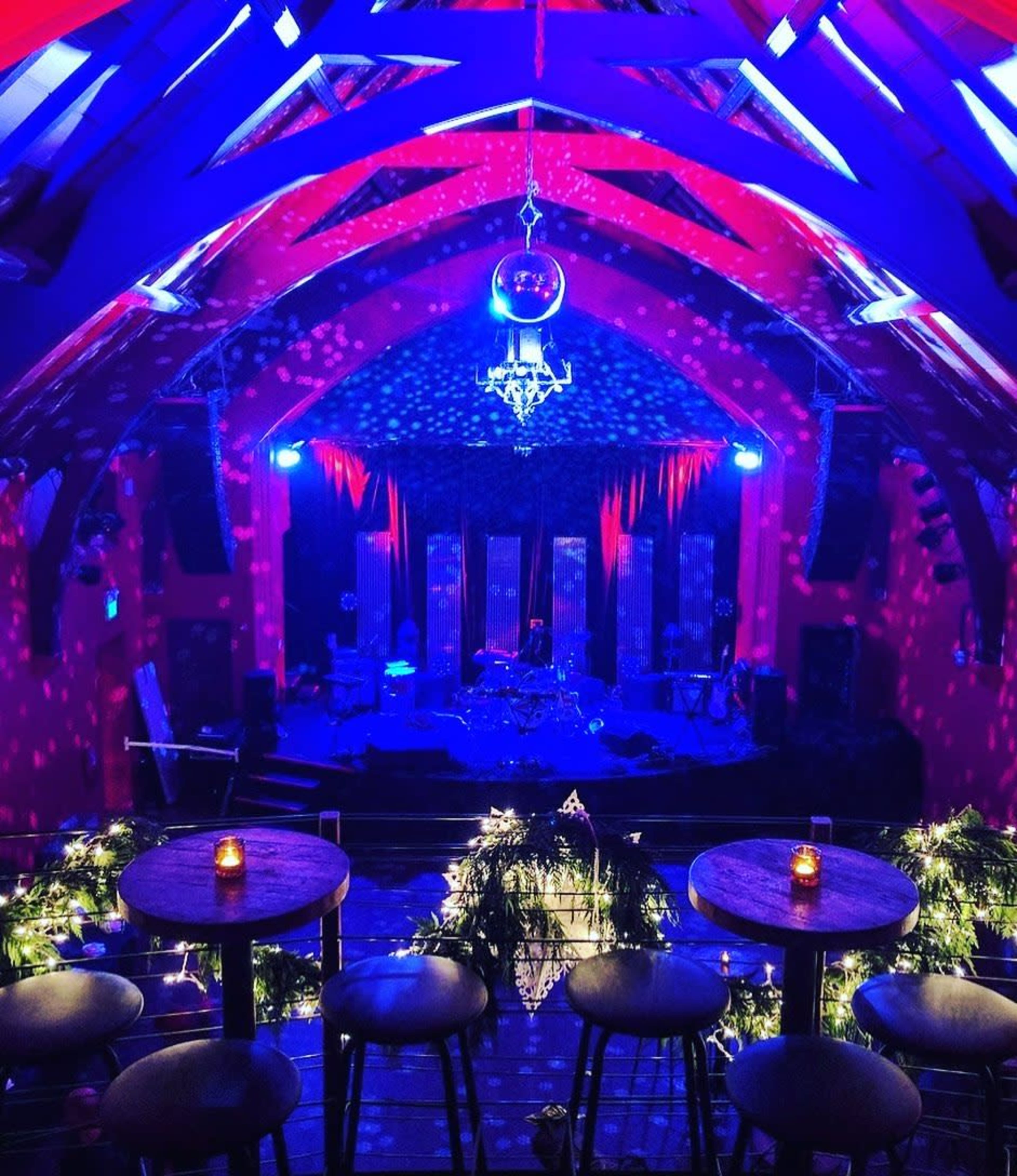 The image shows a vibrant music venue with colorful lighting effects, a stage set for a performance, and tables adorned with candles.