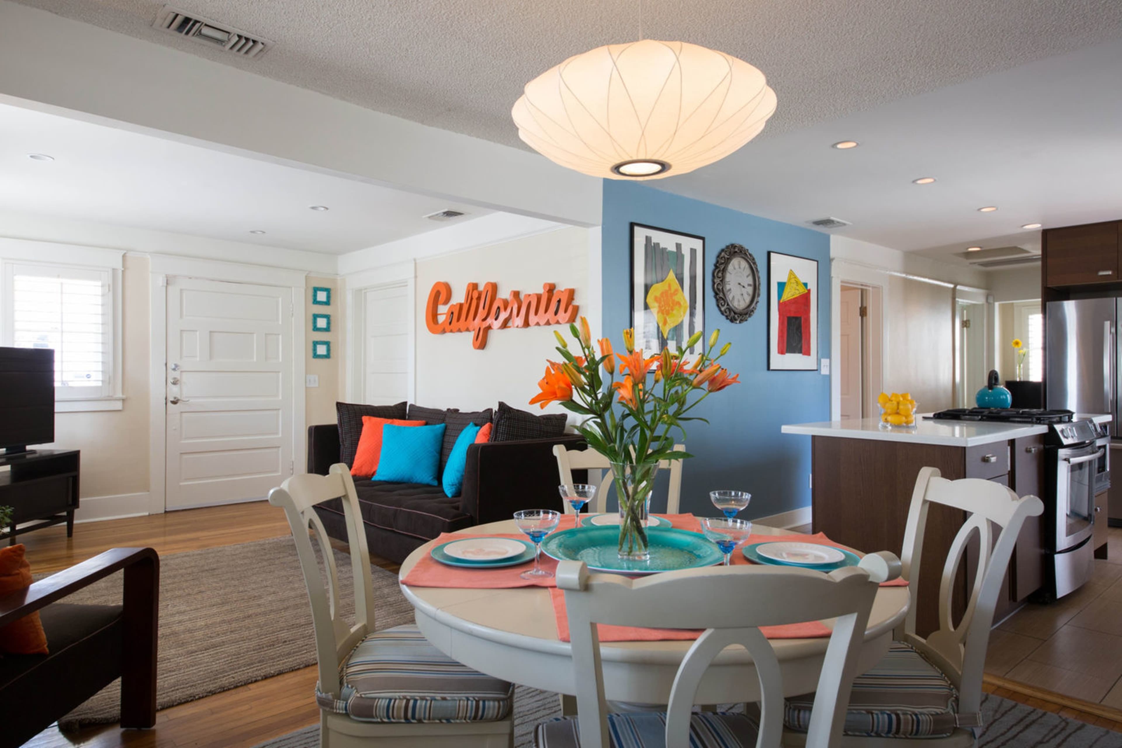 A bright and modern living space features a dining area with a round white table set for four, surrounded by colorful decor and a cozy sofa.