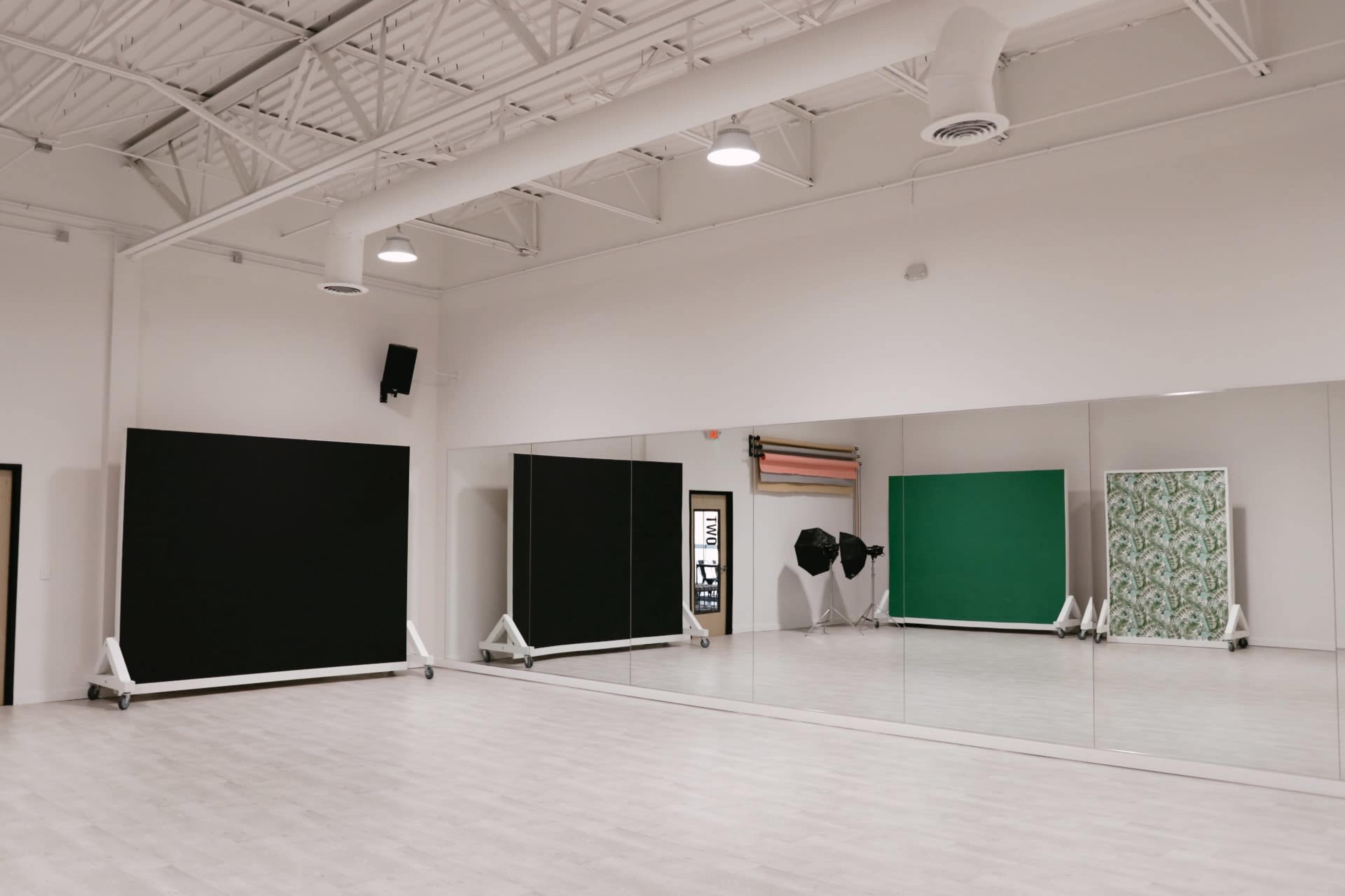 The image shows a spacious photography studio with large mirrors, green and black backdrops, and softbox lighting setups.