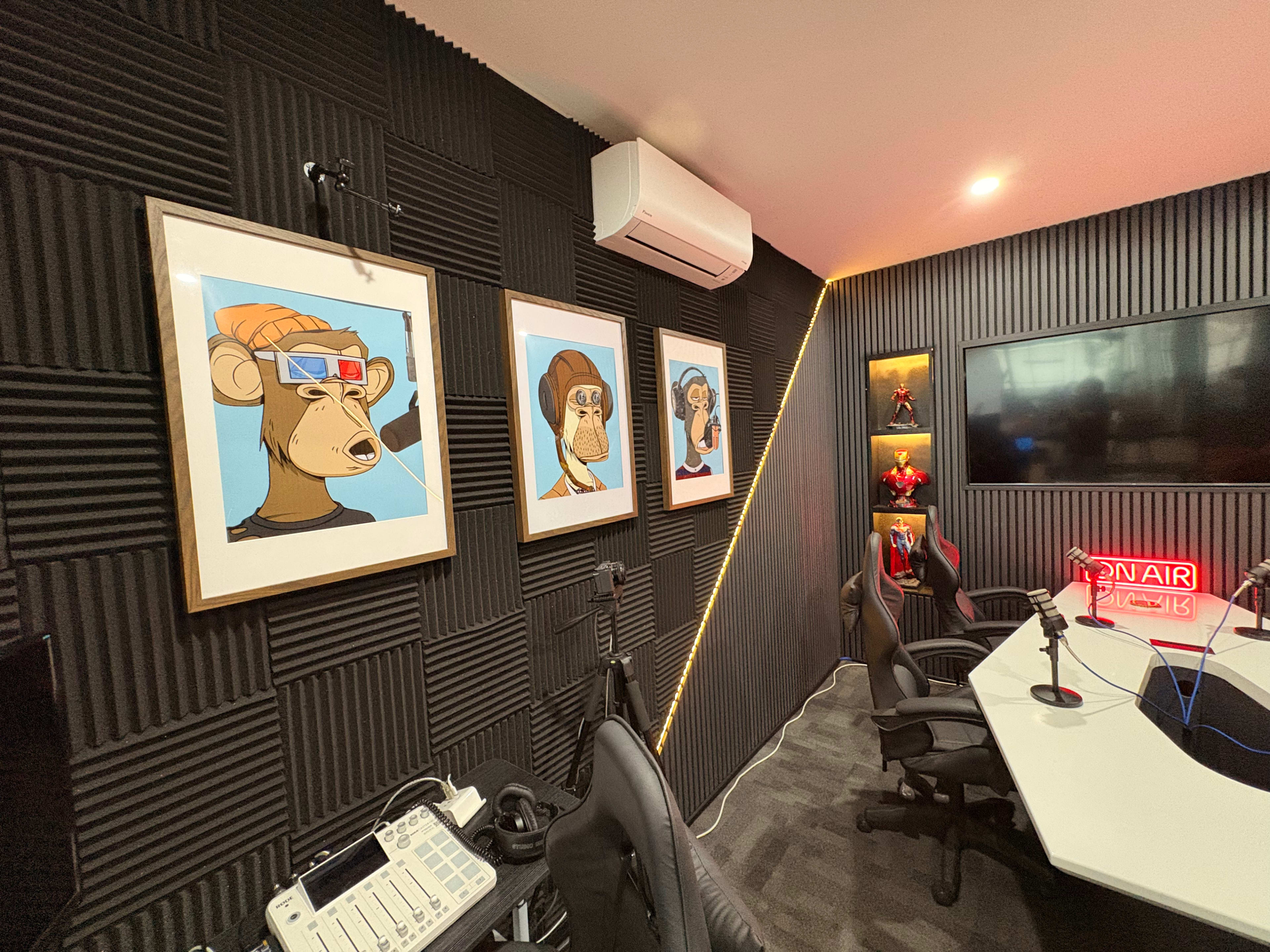 The image shows a modern office or studio space with black textured walls, featuring framed art of stylized monkey illustrations and a neon "ON AIR" sign.