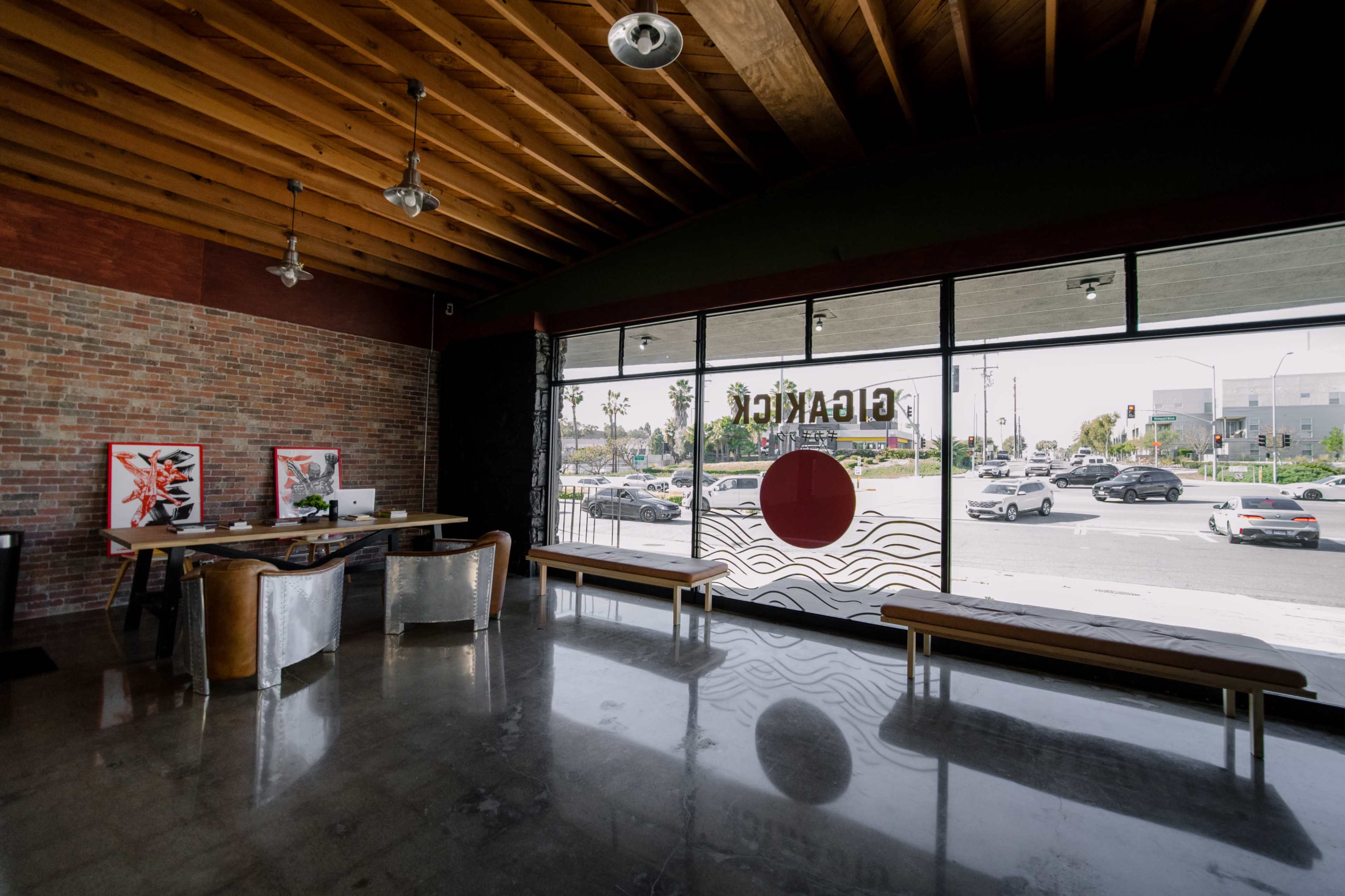 The image shows a modern interior of a business with wooden beams, brick walls, and large windows facing a busy street.
