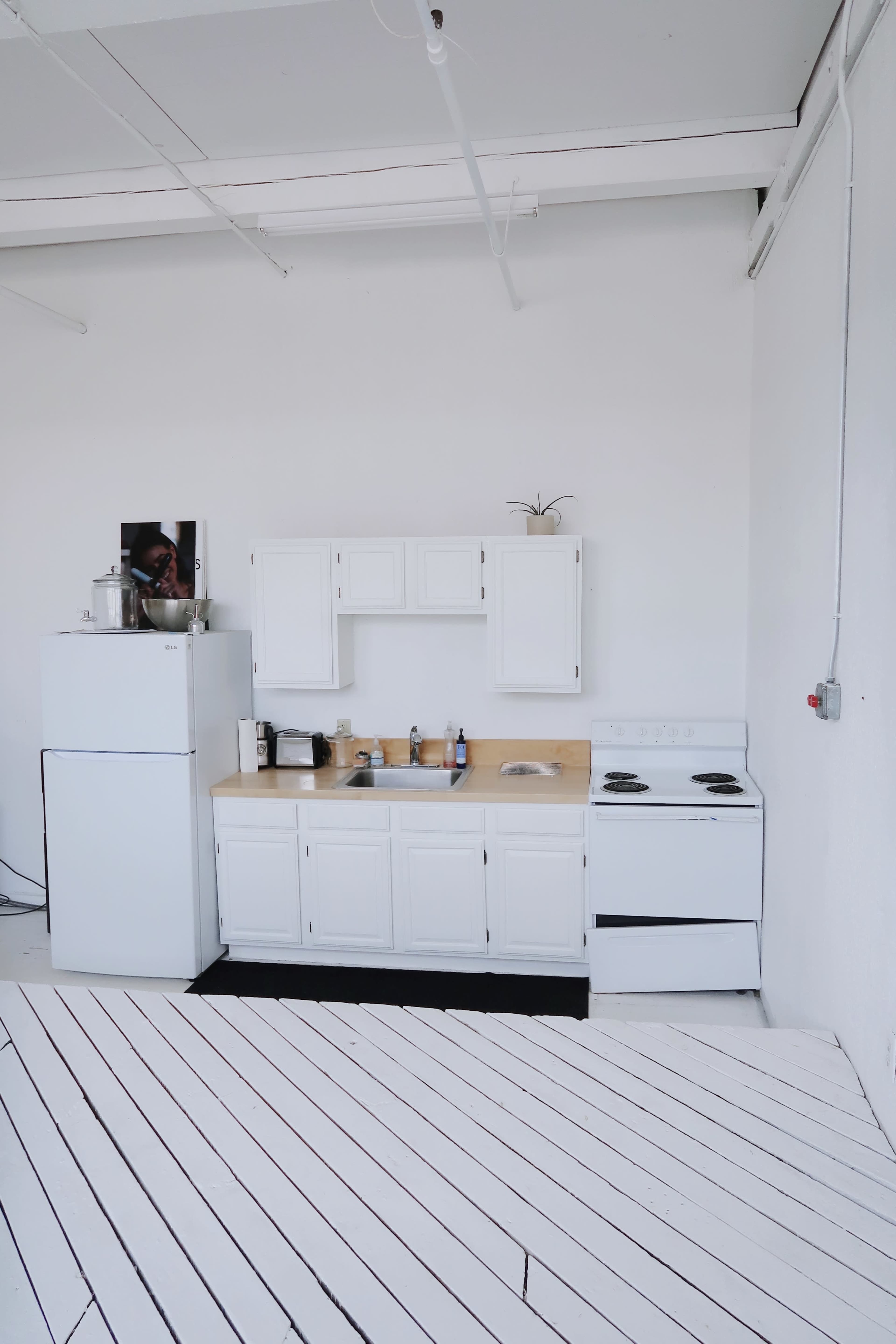 The image shows a modern kitchen with white cabinetry, a wooden countertop, a stove, and a refrigerator against a white wall and floor.