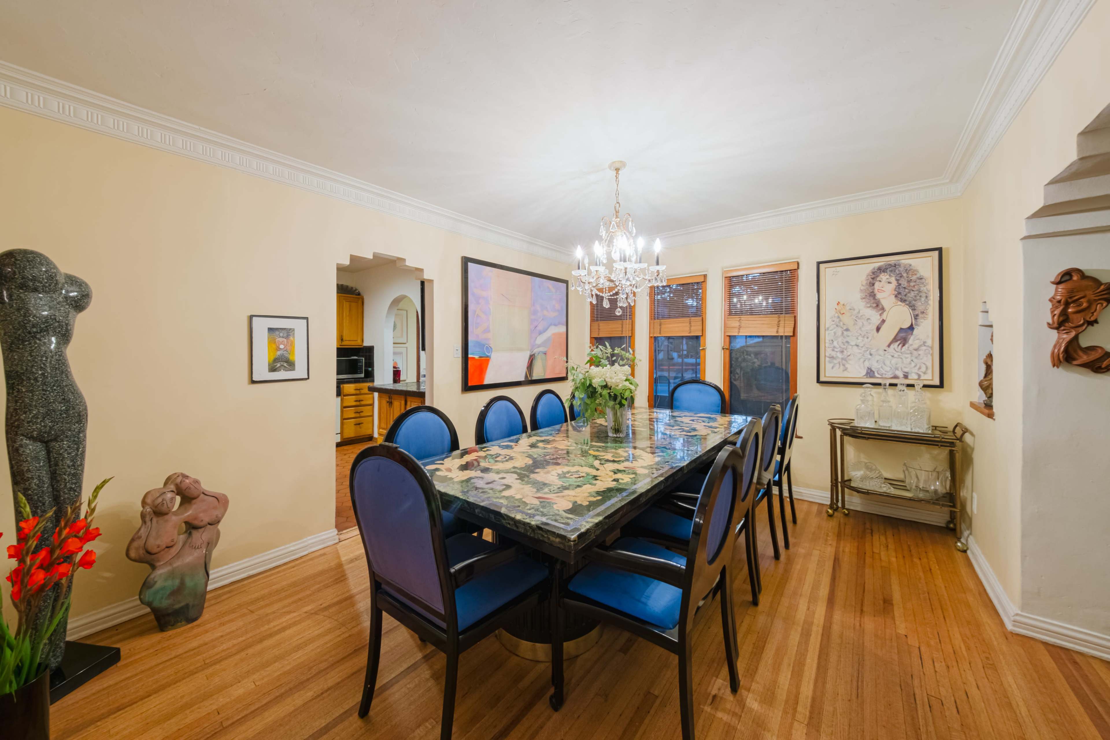 The dining room features a long table surrounded by blue chairs, with framed artwork on the walls and sculptures accentuating the space.