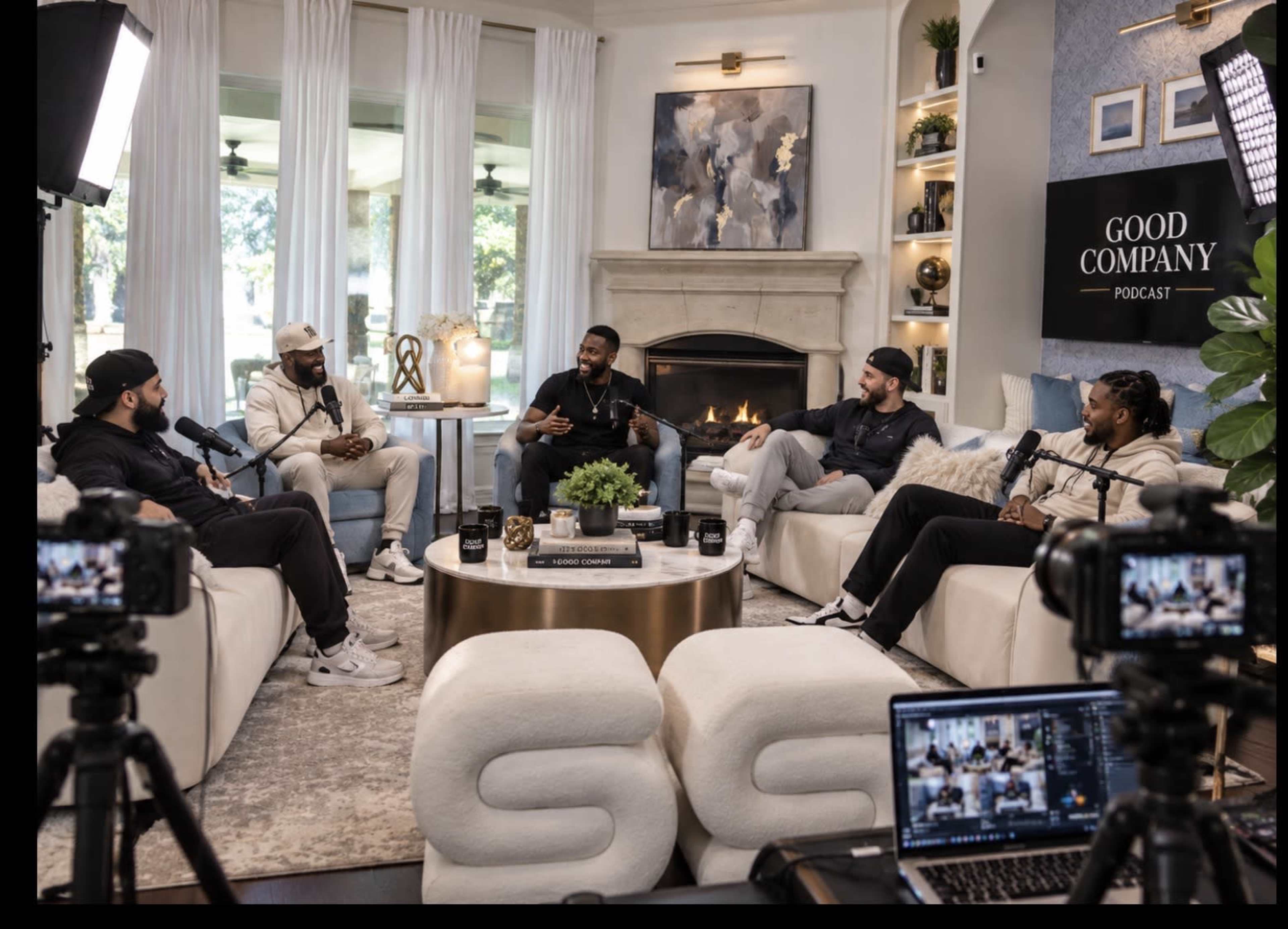 A group of five men is seated in a modern living room setting, engaged in a discussion while microphones and cameras are set up for a podcast.