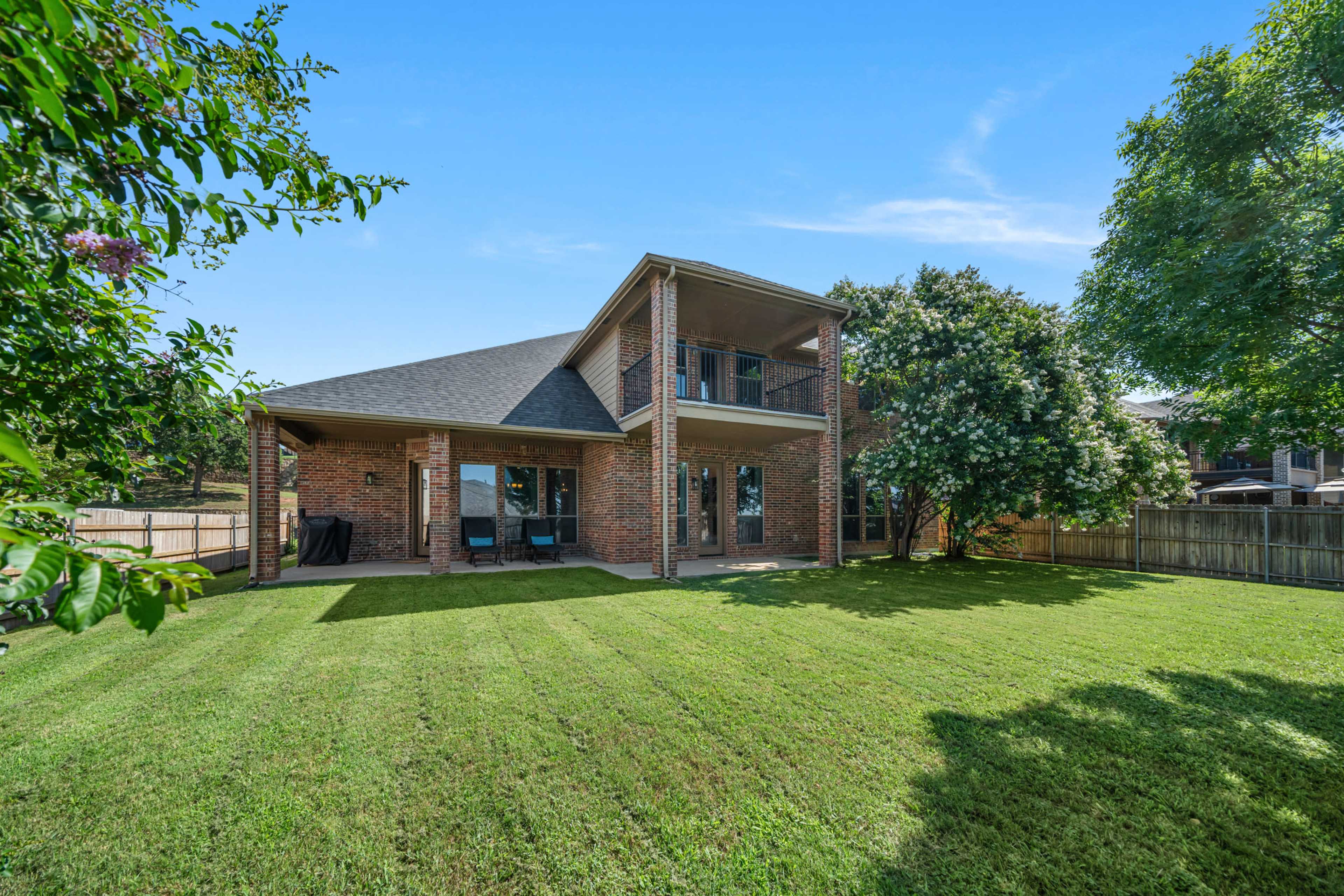 The image shows a two-story brick house with a well-maintained lawn and a patio in the backyard.