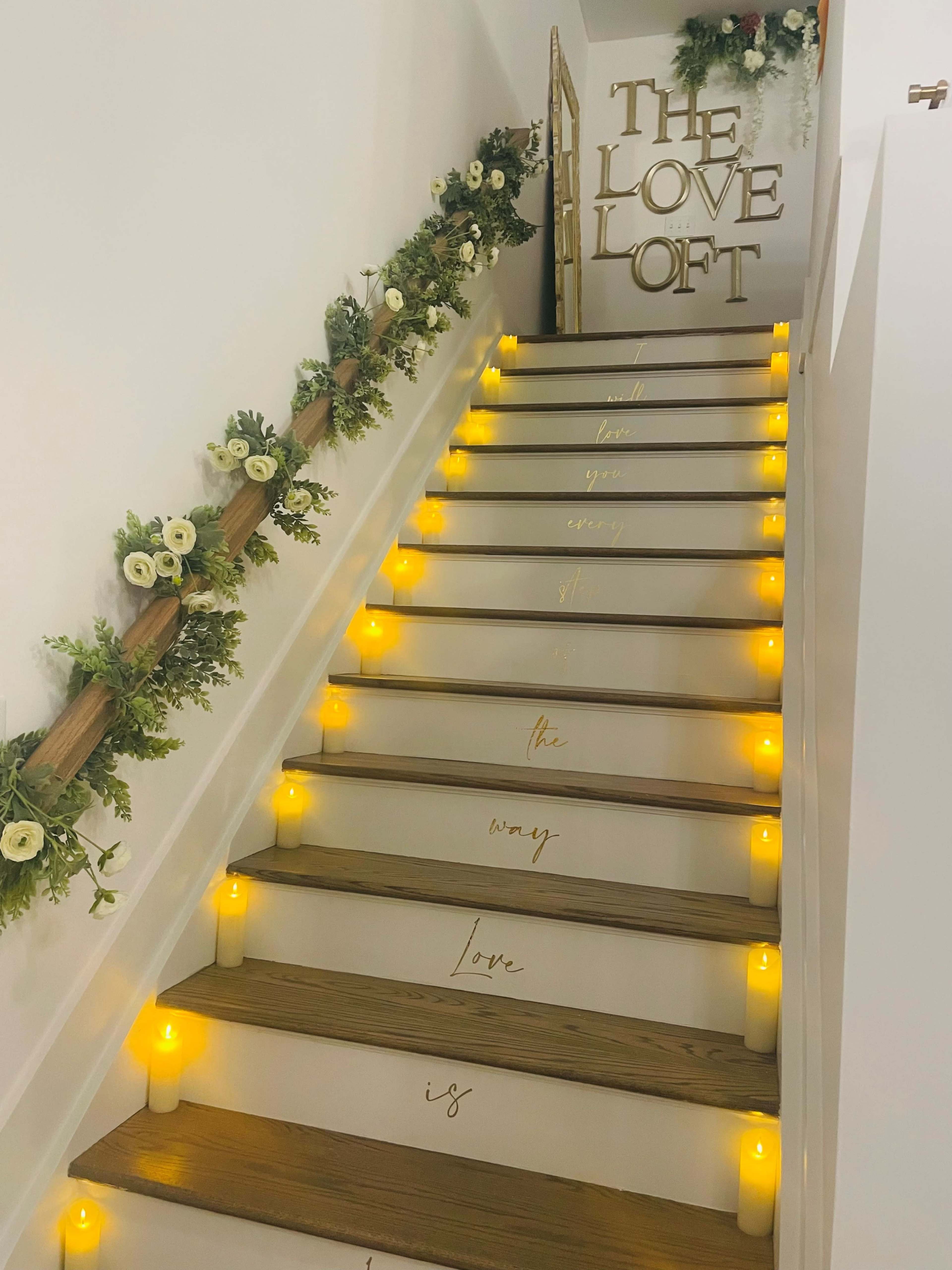 A staircase adorned with greenery and candles features the text "The Love Loft" and a message written along the steps.