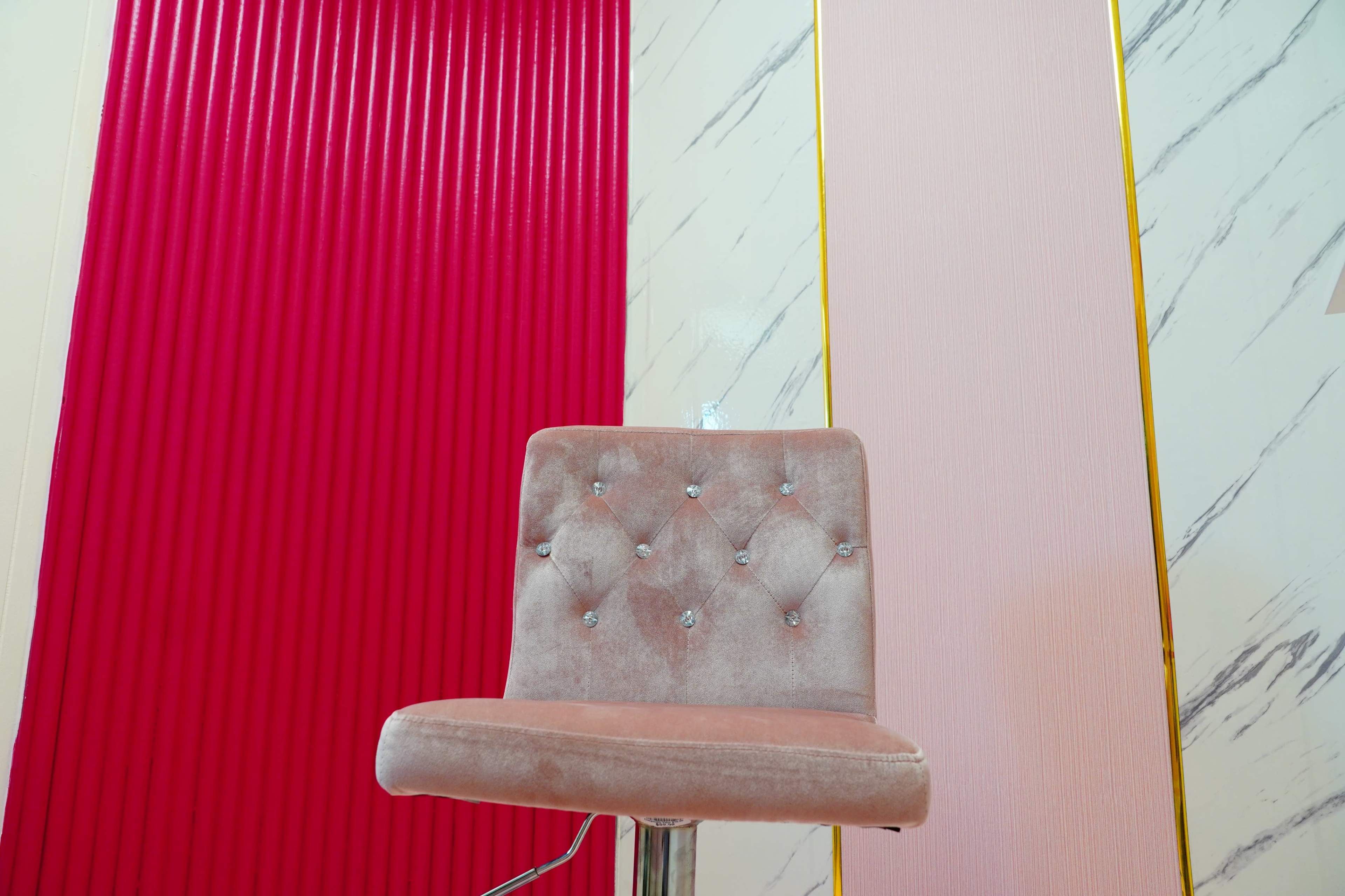 A velvet chair with a tufted design is positioned in front of textured red and pink walls.